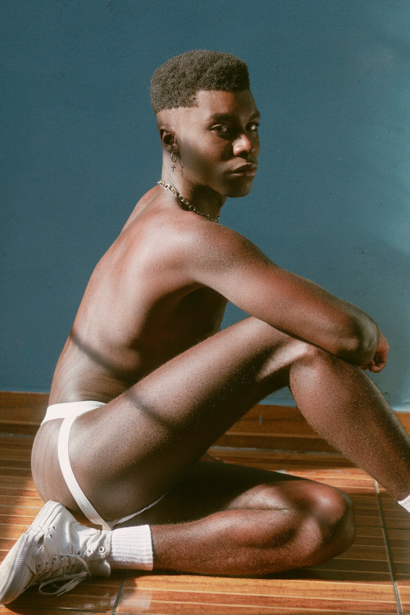 a boy sitting sideways wearing a jock strap and converse