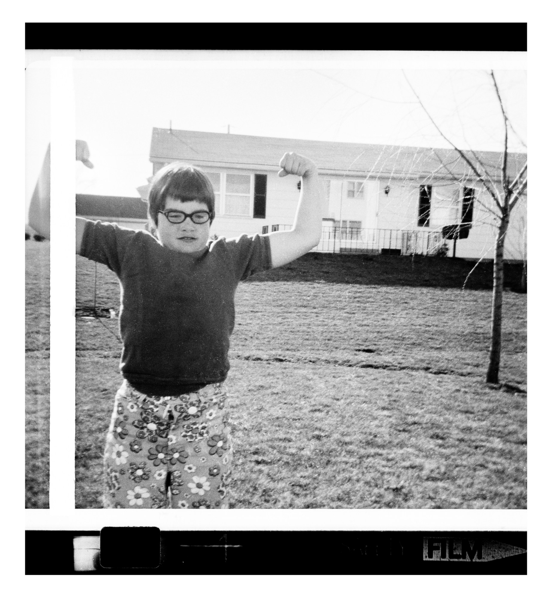 a self-portrait of a young catherine opie flexing her biceps in a garden