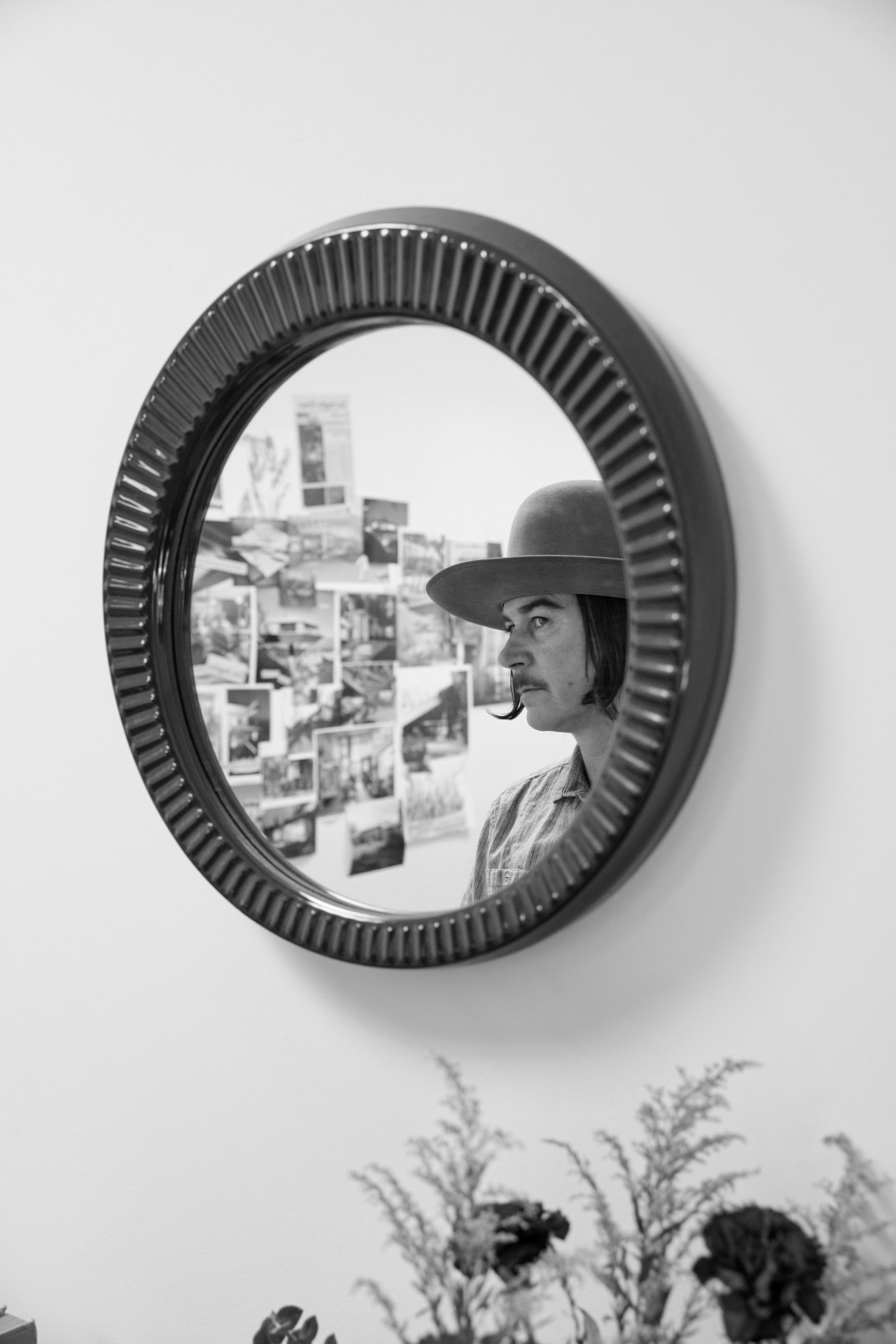 a person with a moustache looks into a round mirror