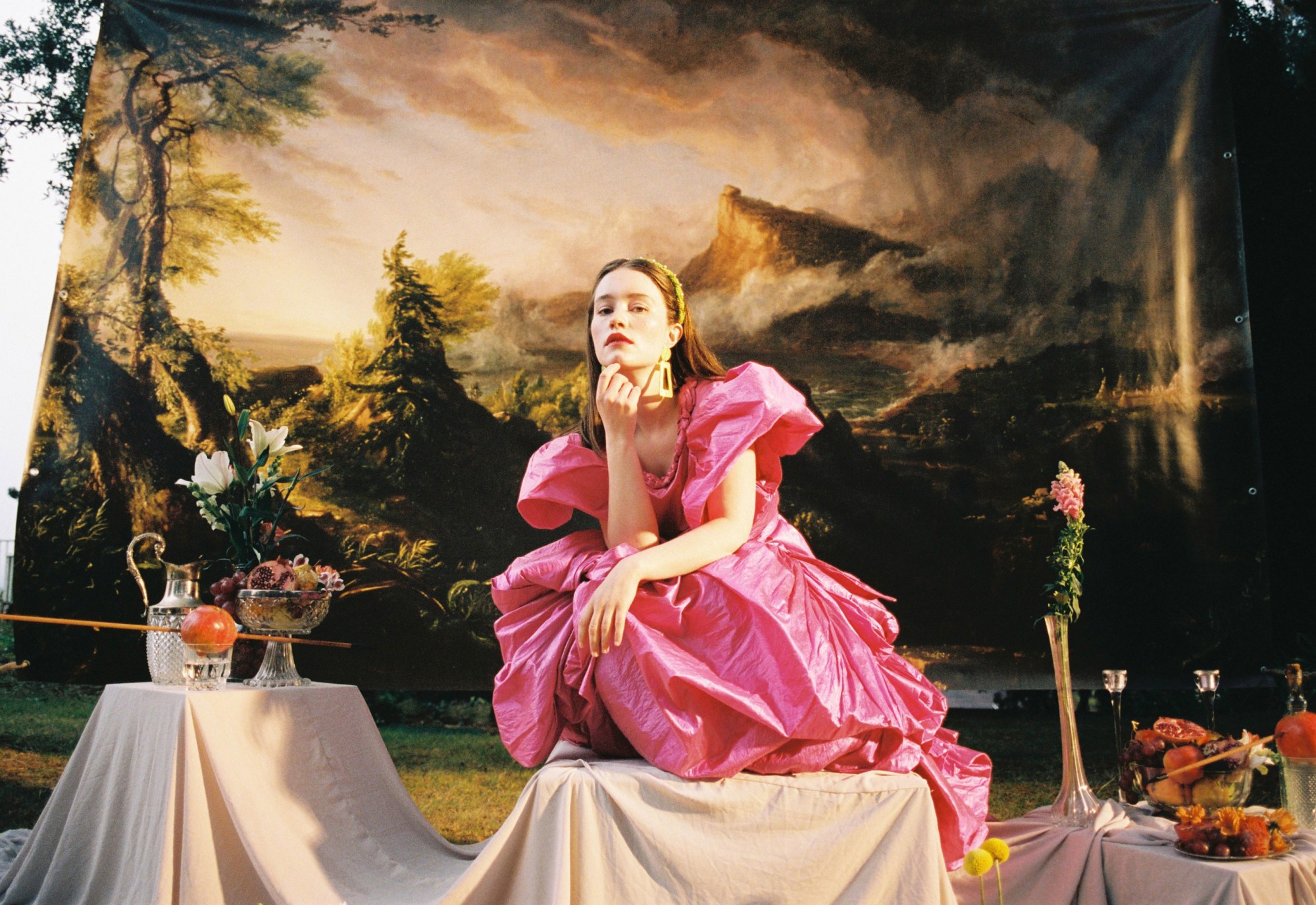 Sigrid wearing a big pink dress, crouching down in front of a scenic painted landscape