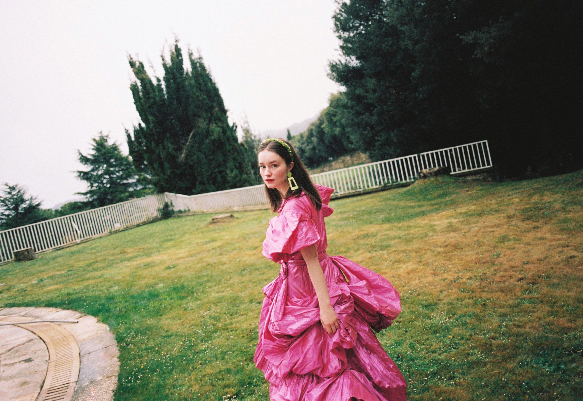 Sigrid in a pink dress in a garden, looking over her shoulder to camera