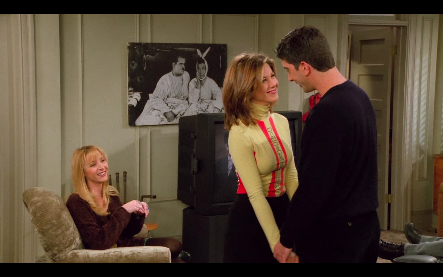 Jennifer Aniston as Rachel Green in Friends wearing black shorts over tights and yellow and red rollneck top.