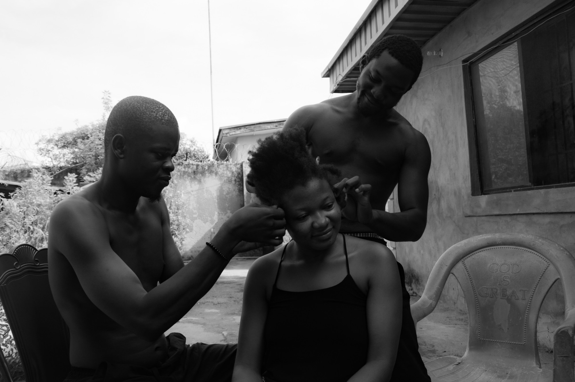 Two men in Nigeria braiding a woman's hair.