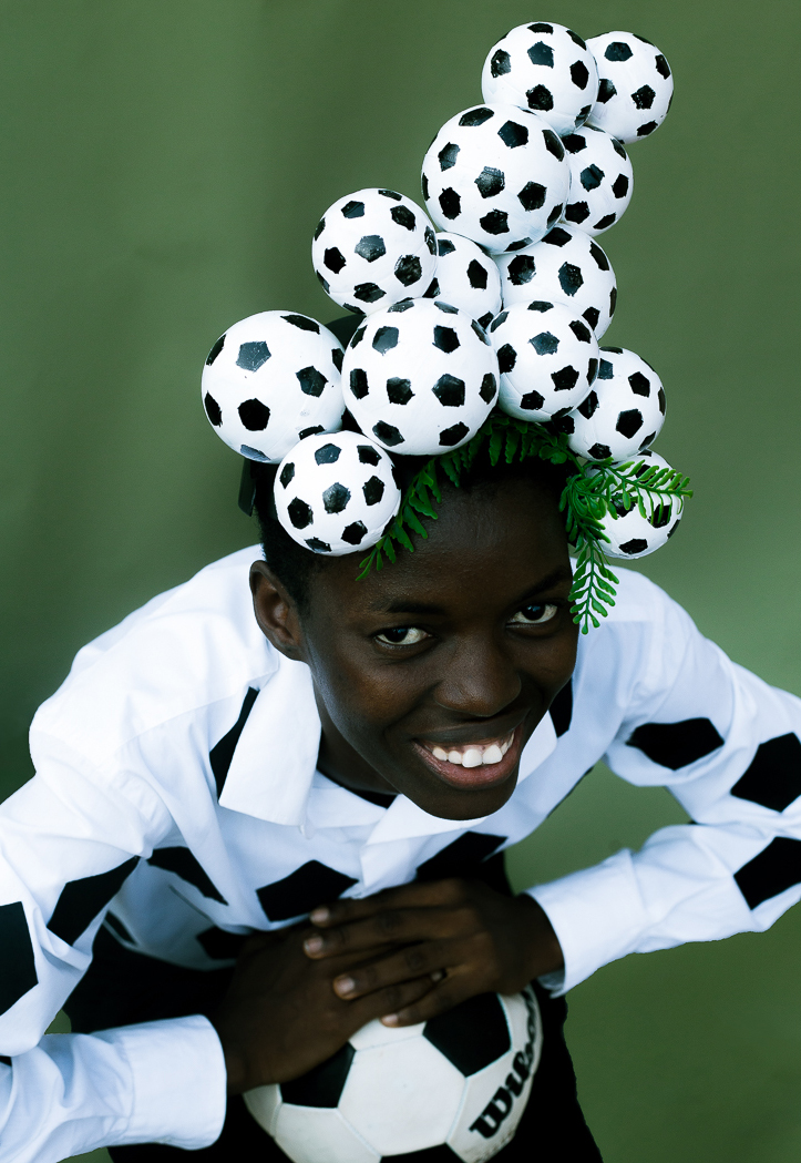 a young boy holding a football and wearing a football sculpture on his head