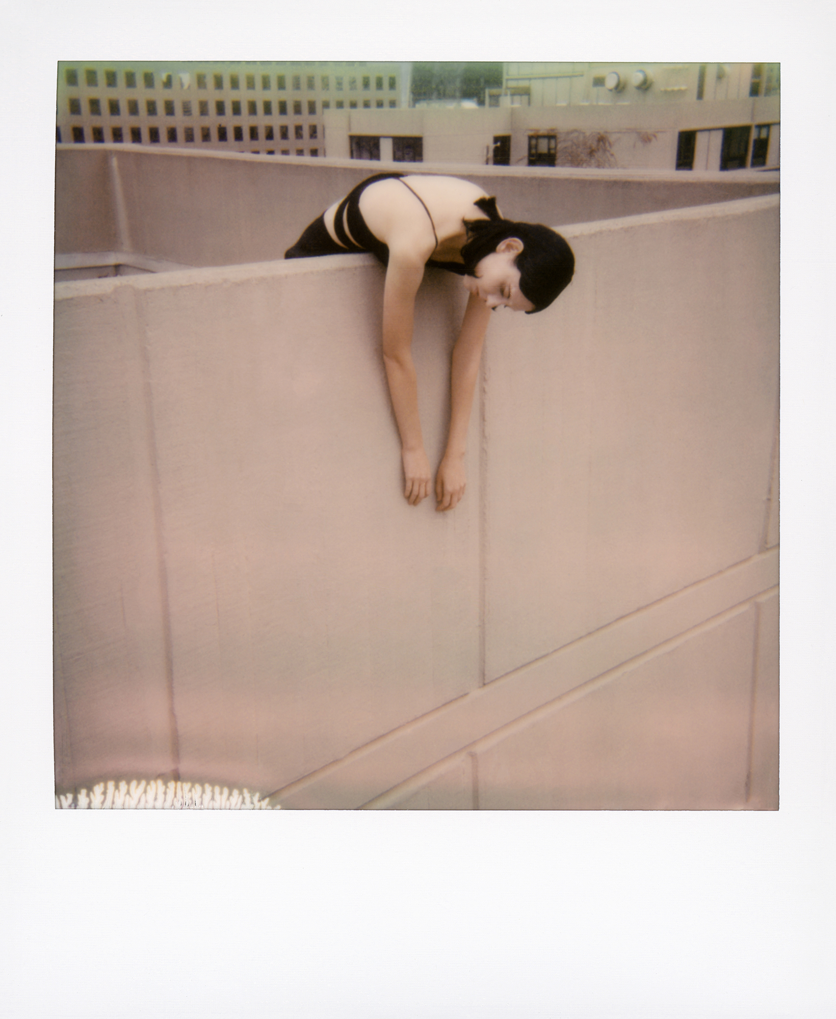 Colour polaroid of a model hanging over a grey building