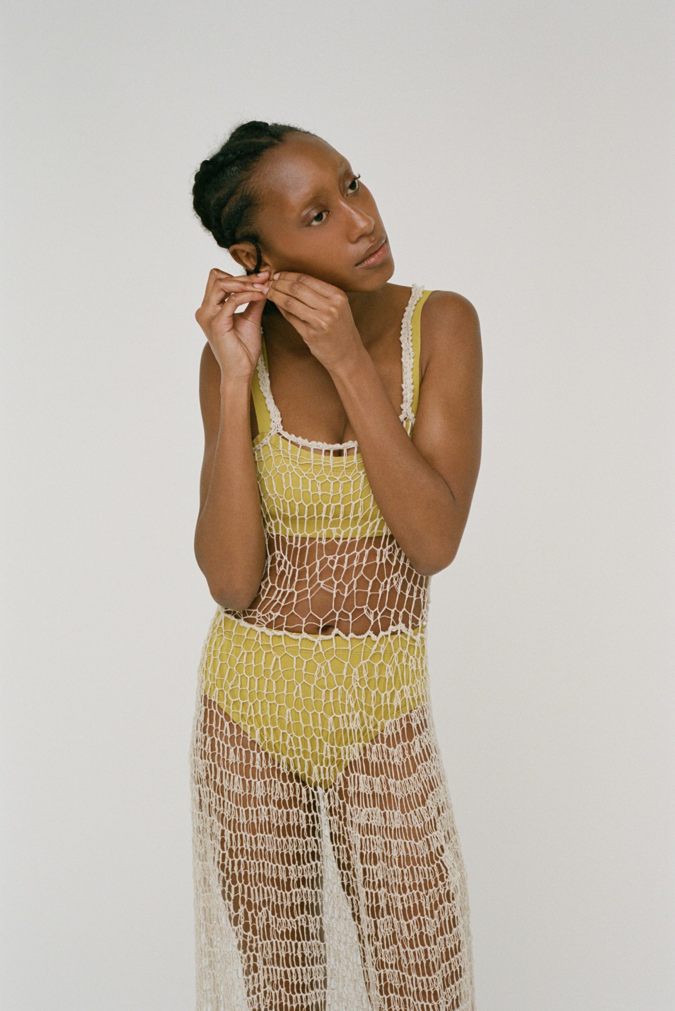 a model putting an earring in wearing a sheer crochet dress