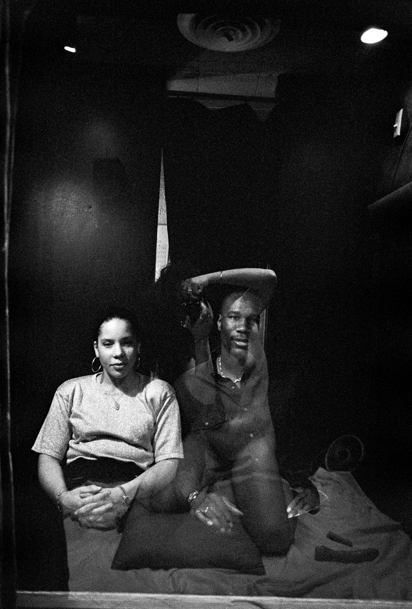 a man and a woman sit inside a pleasure booth while the photographer can't be faintly seen in the reflection