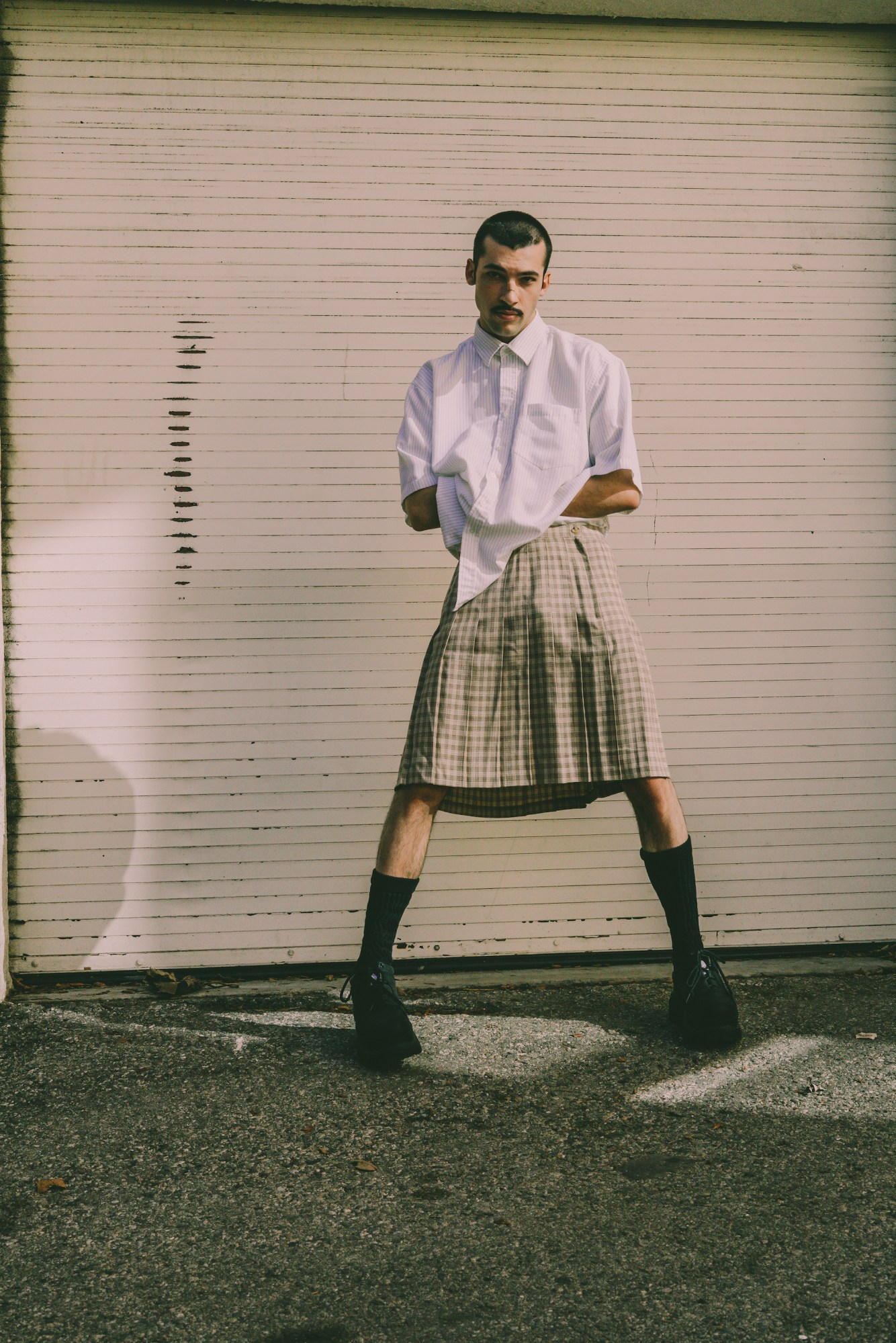 leo reilly posing in a plaid skirt and white button up shirt