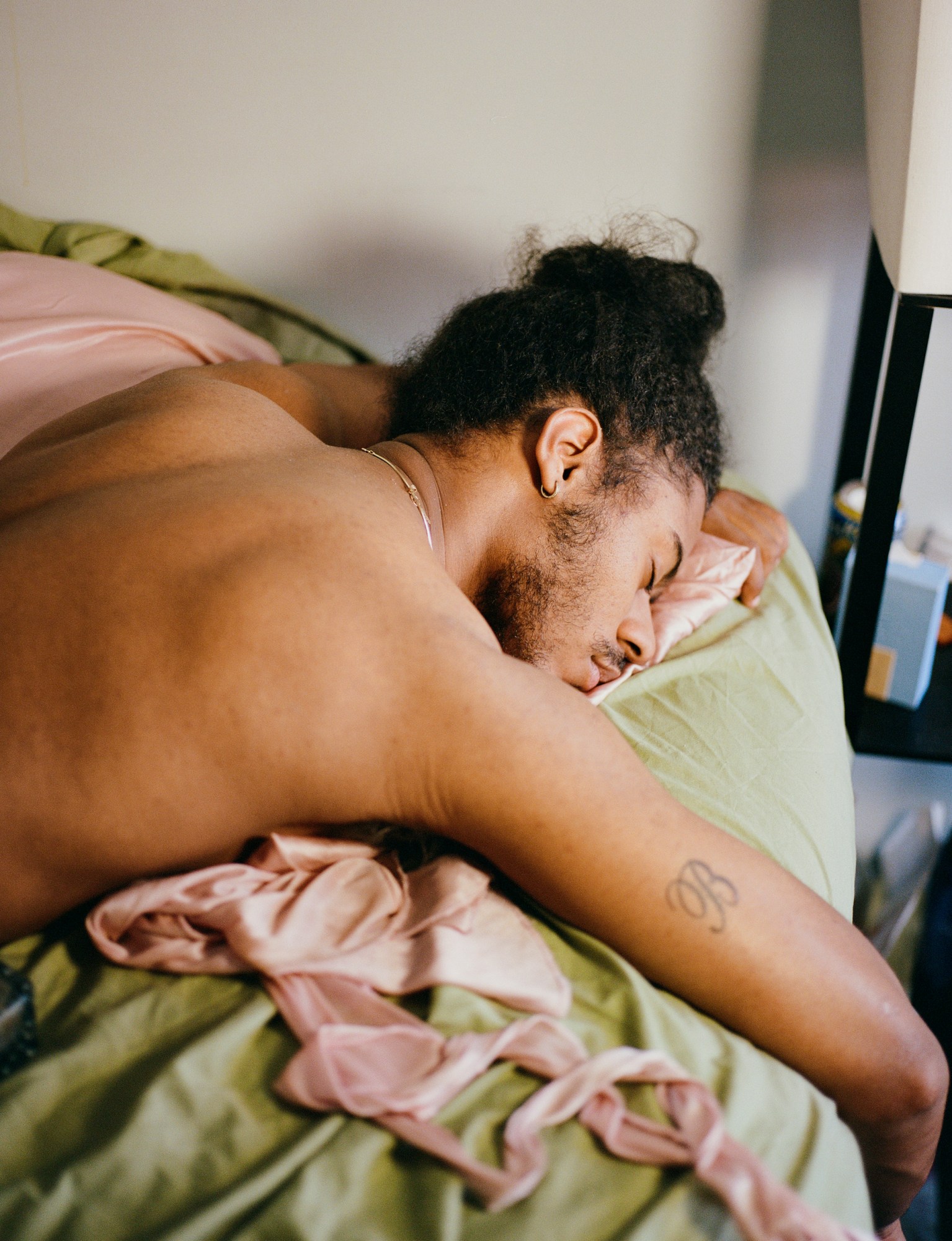 portrait of a man lying in bed with a B tattoo by kadar small