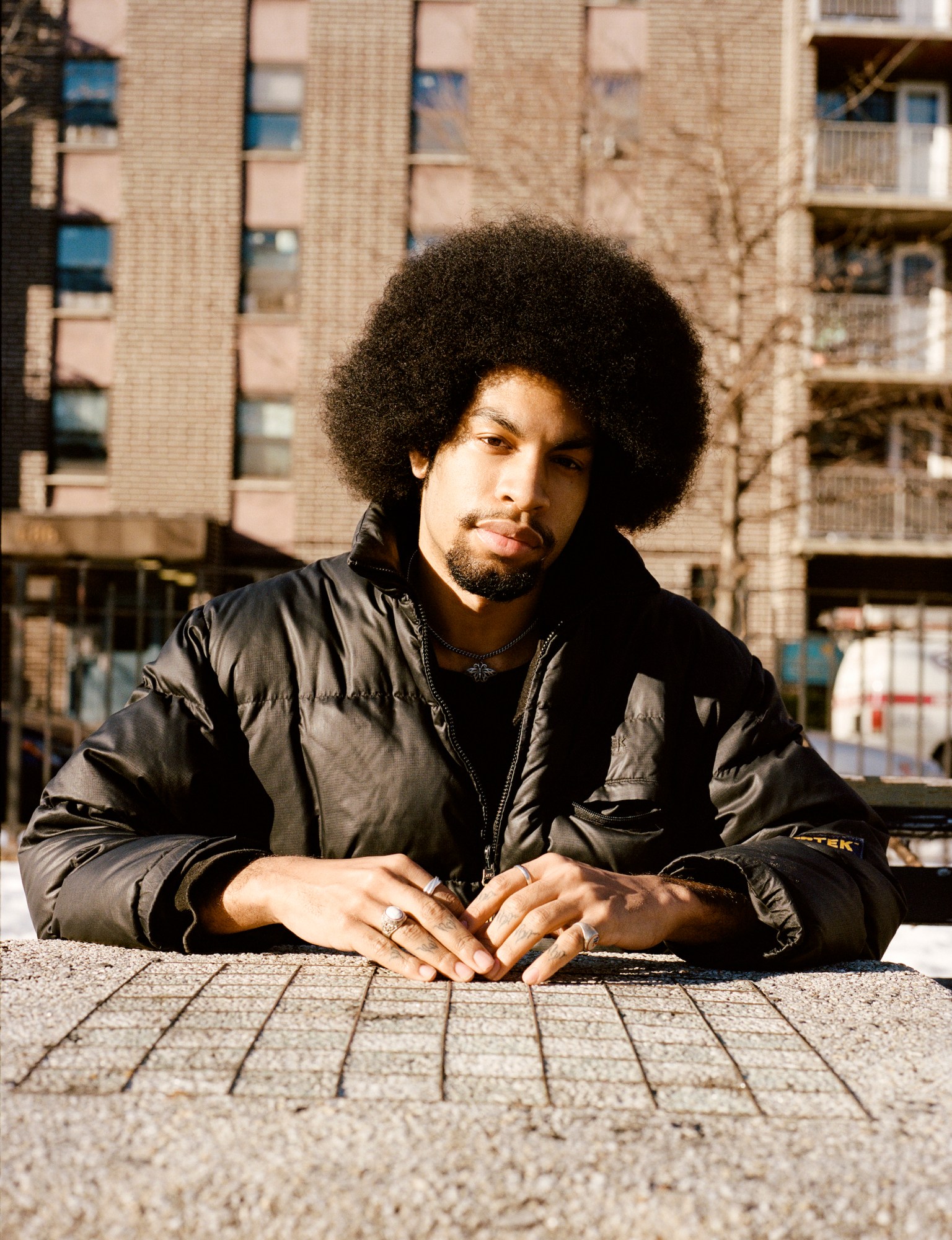 a man with an afro sitting at an outdoor chess table by kadar small