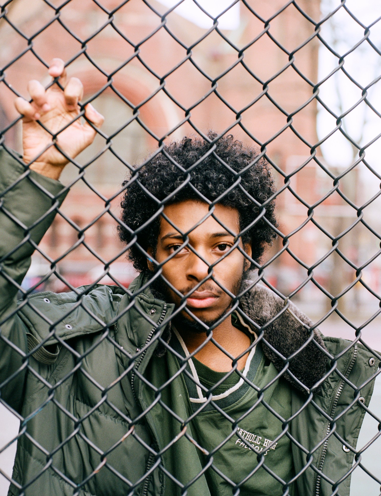 a man standing behind a chainlink fence with his hand reaching up by kadar small