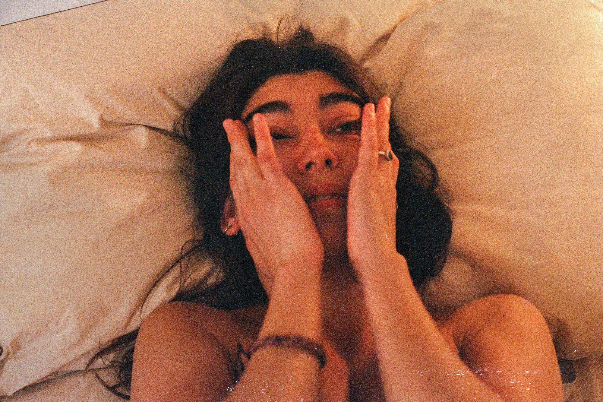 a woman rubs tears from her eyes lying on a bed