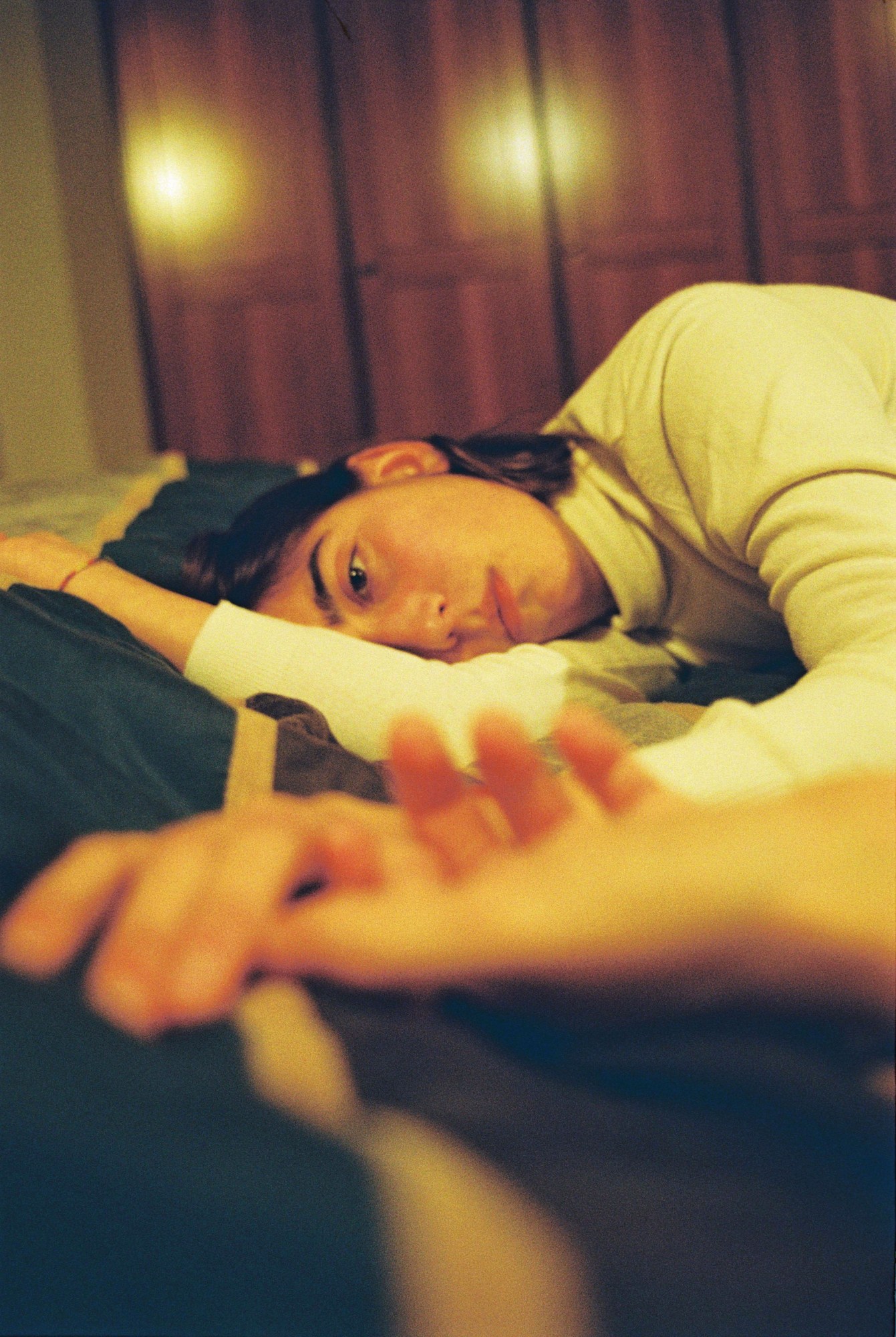 a woman lies on a bed holding the photographer's hand