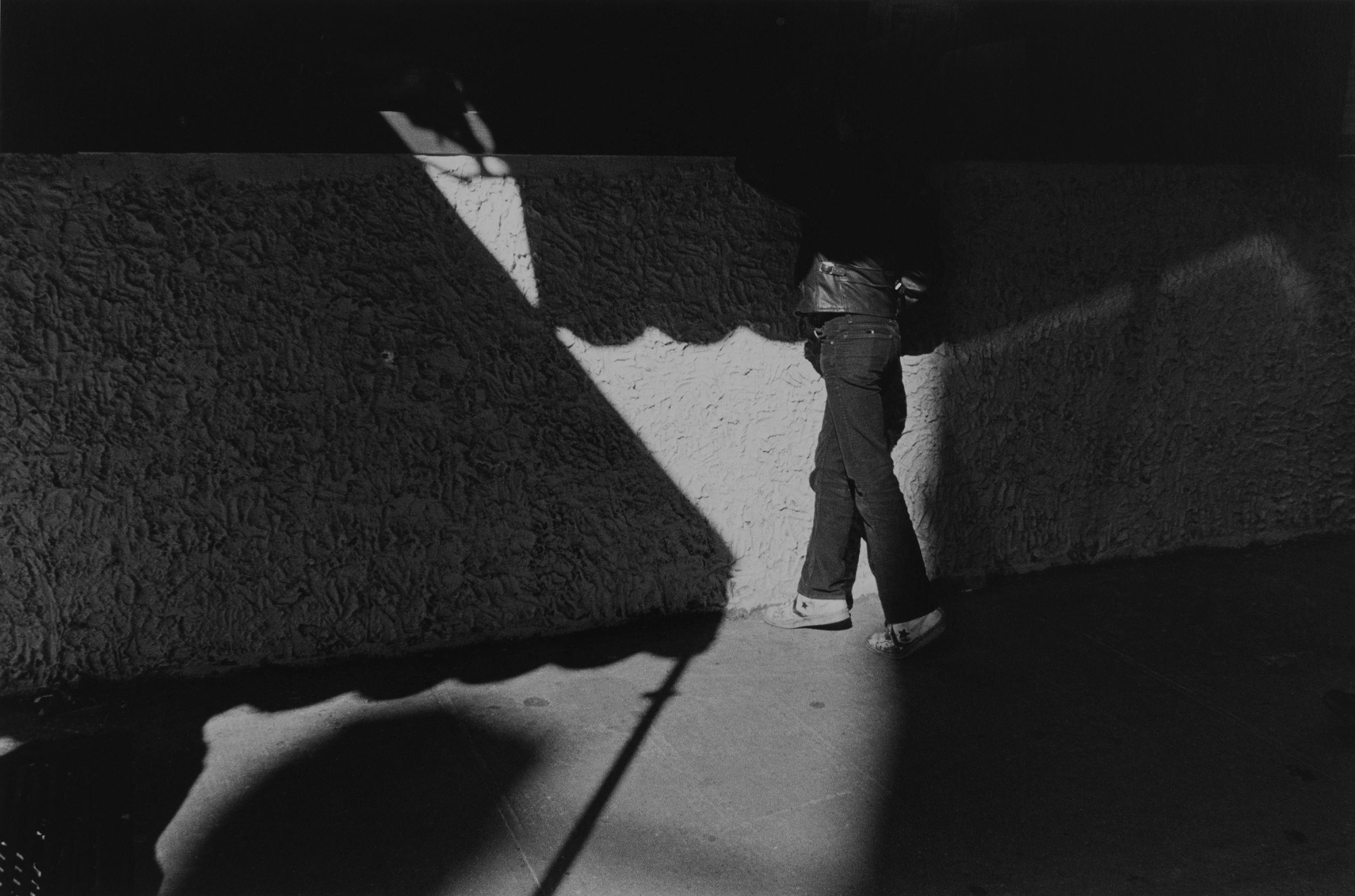 a man's legs can be seen in the gap between shadows on the street