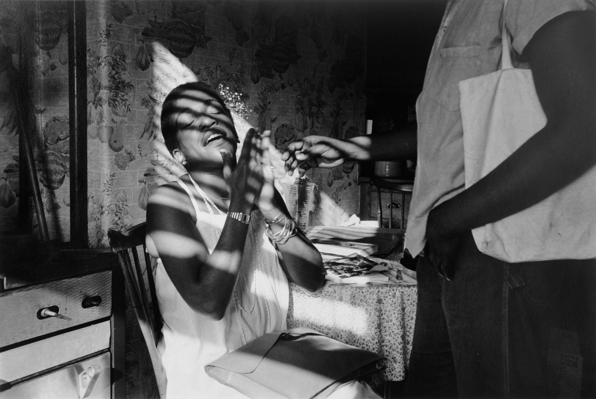 a woman is sat down with shadows from shutters across her face holds her hands up