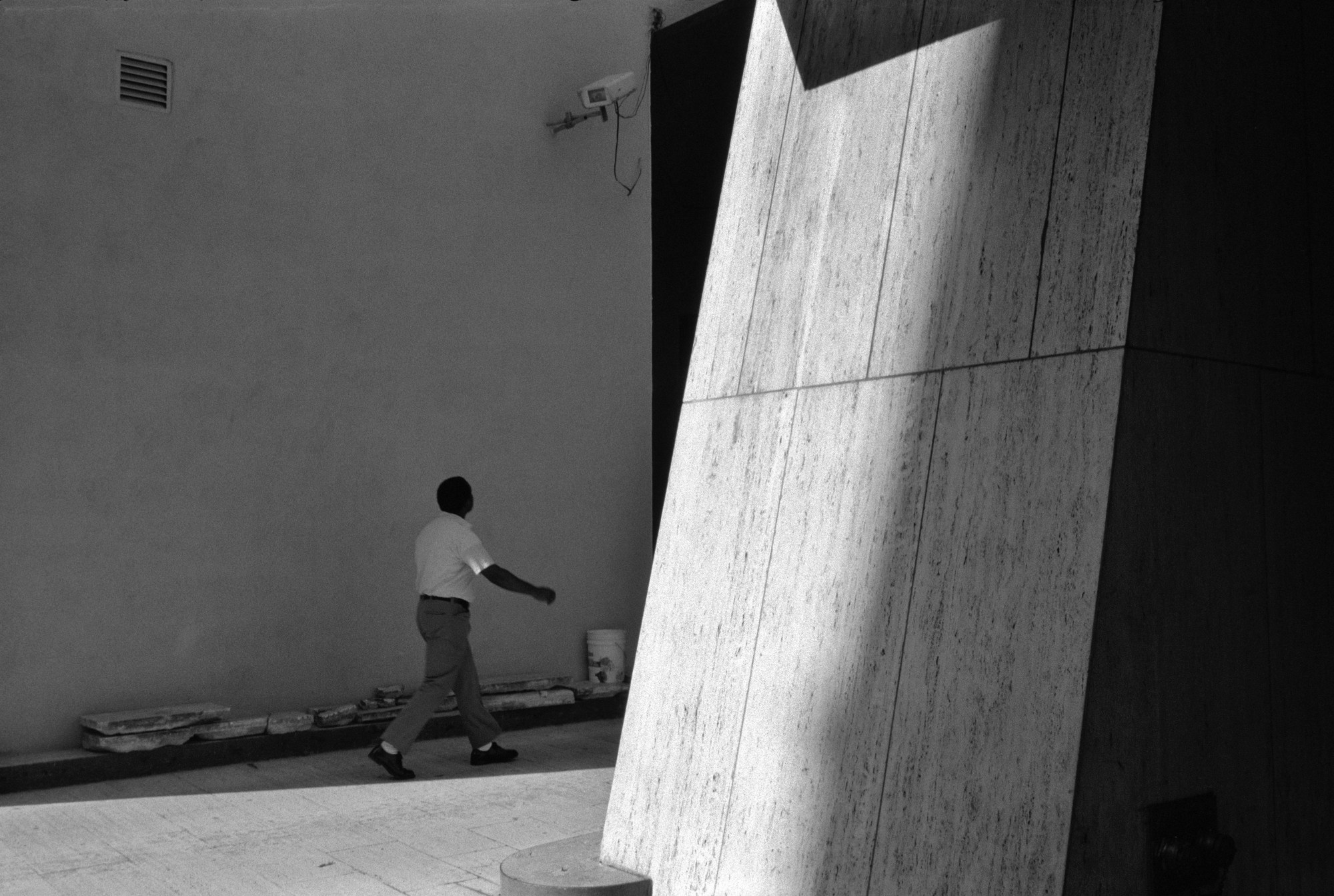 a man strides along a road, framed by shadows and light again white walls