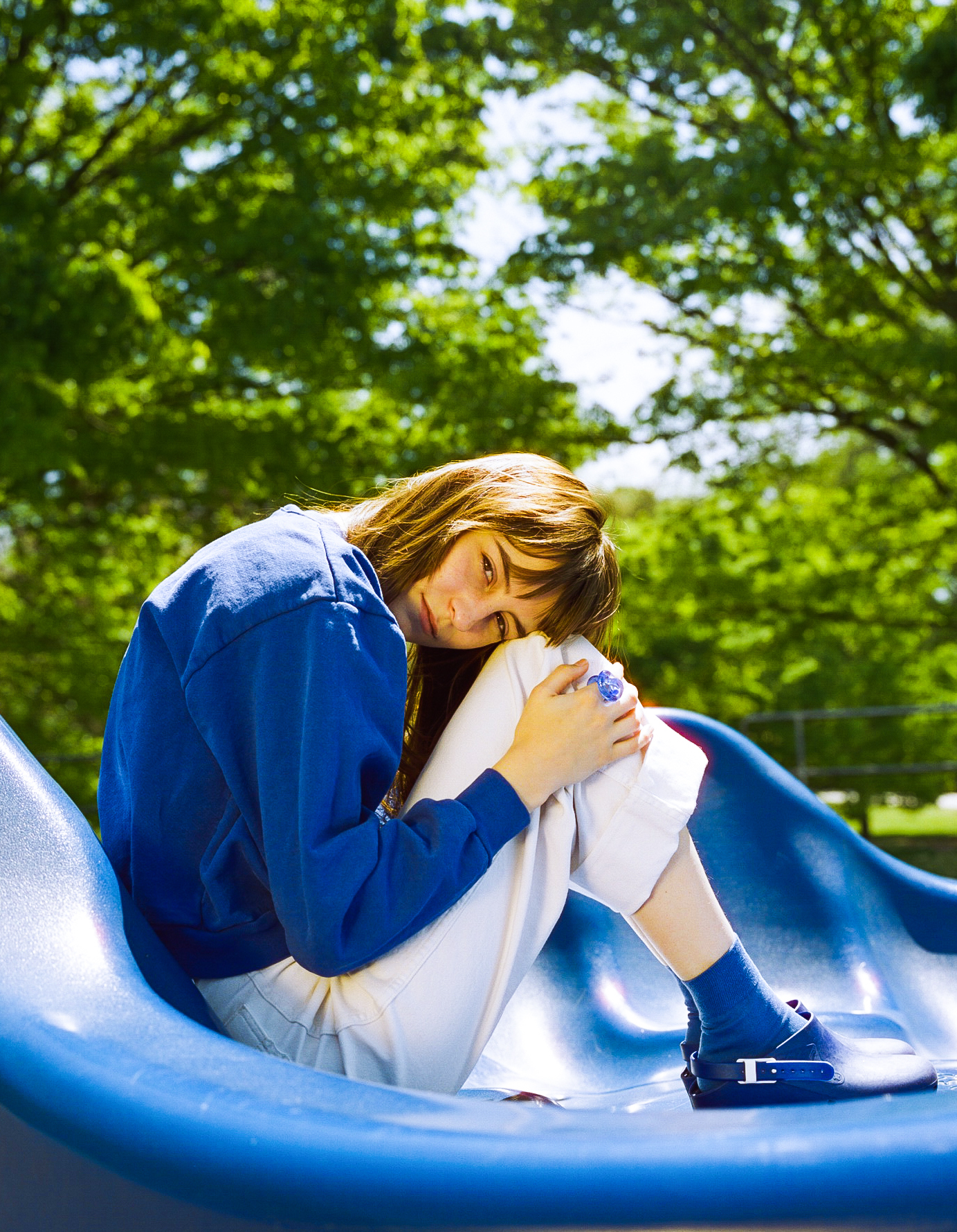 Faye Webster sitting curled up in a ball on a slide outside