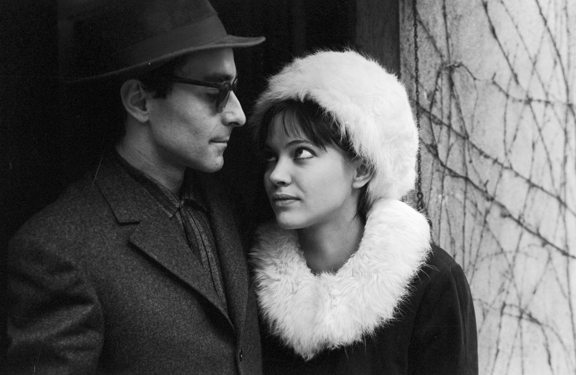 anna karina looking up at jean-luc godard while wearing a fur trimmed coat and hat