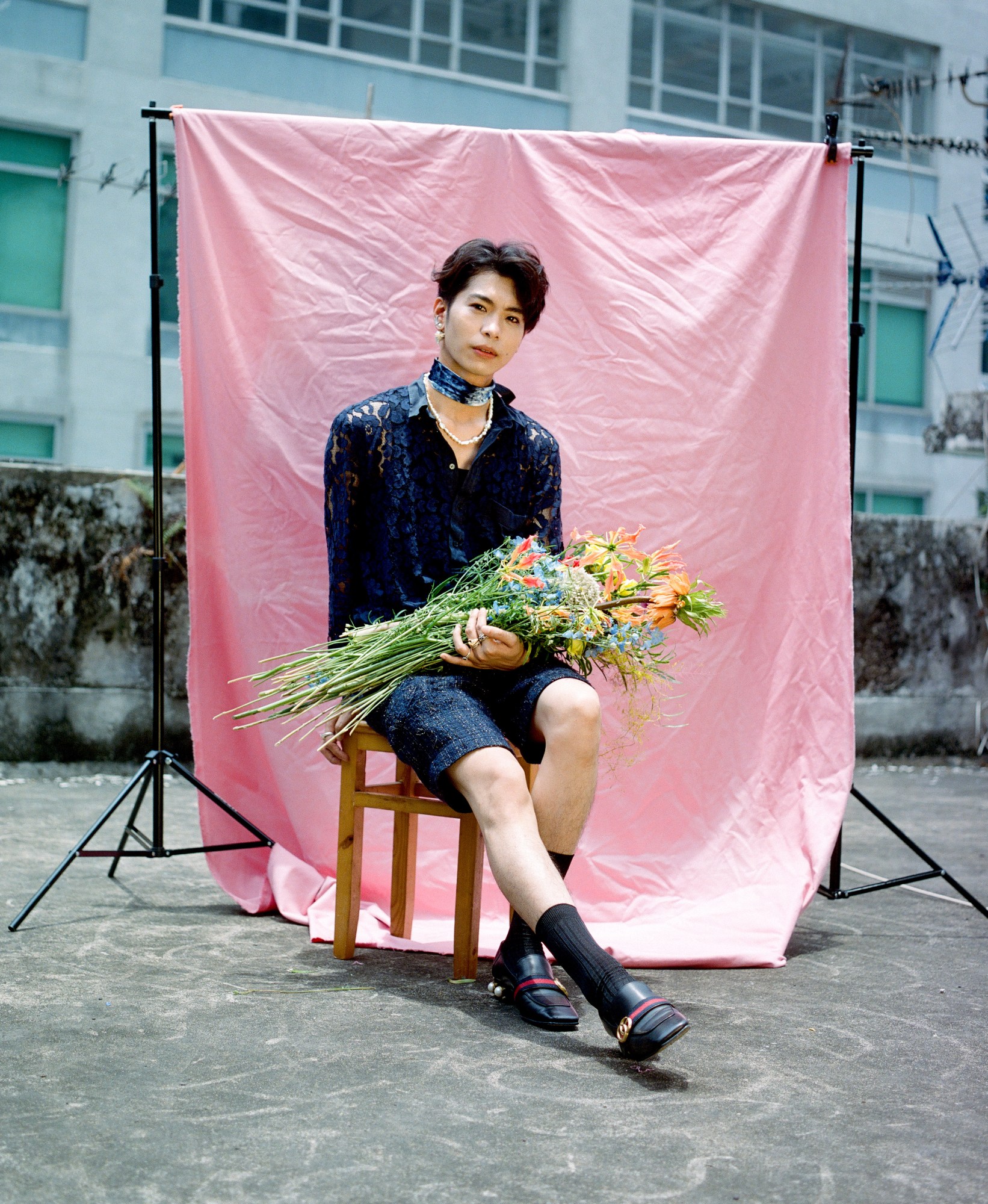 a portrait of mite sitting on a chair in front of a pink background and holding flowers