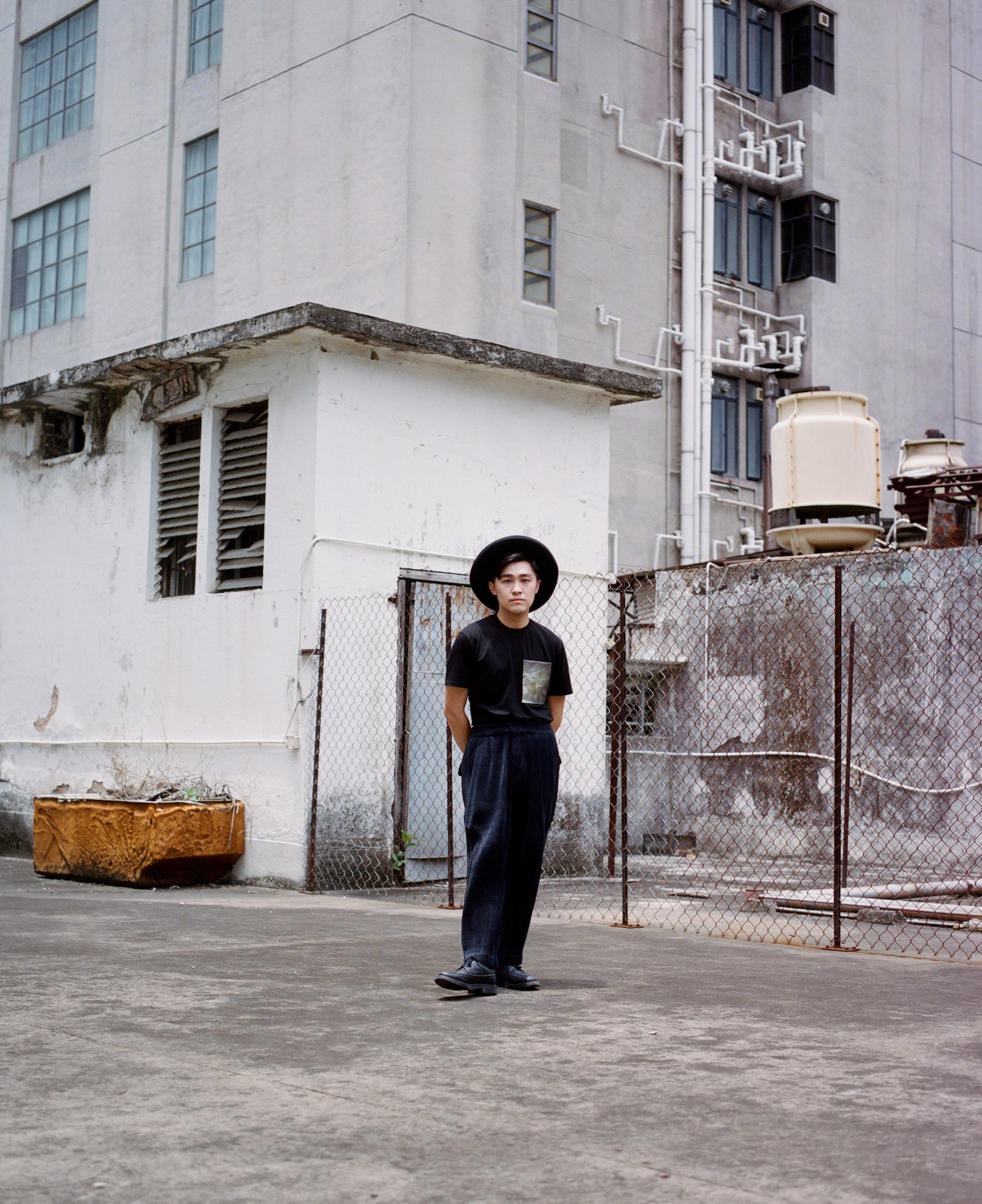 derek chan standing in front of a chainlink fence inhong kong