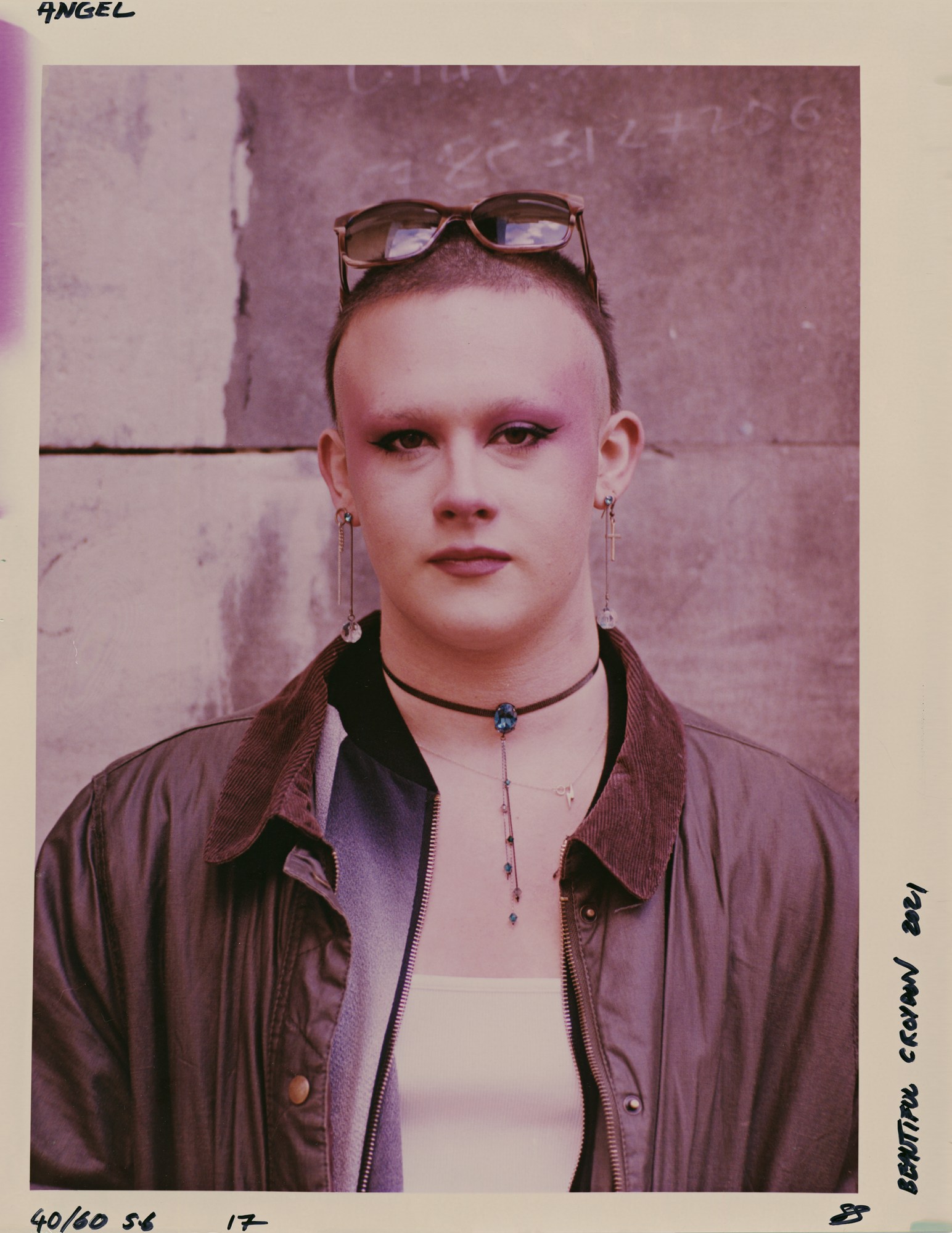 a person with a shaved head, lots of jewellery and heavy makeup, wearing a barbour jacket