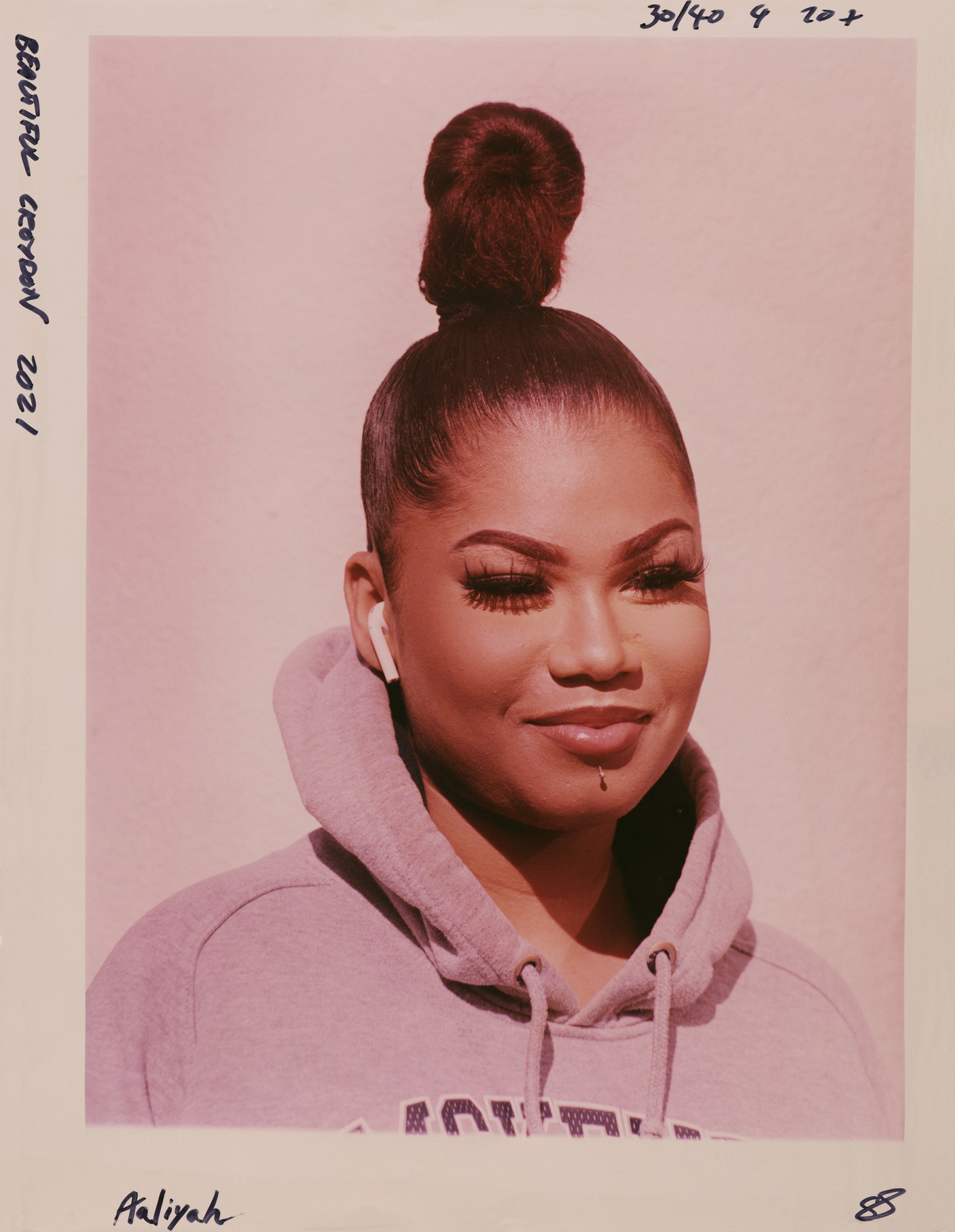 a woman wearing a grey hoodie, airpods and her hair tied up in a tight bun