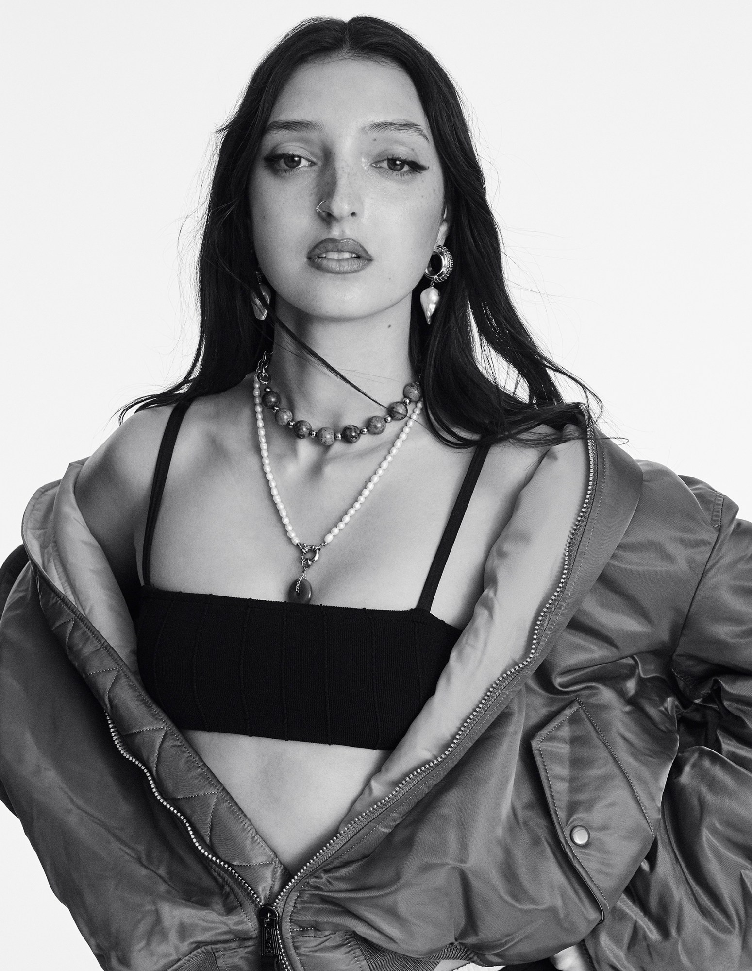 a black-and-white portrait of UK musician LOLA wearing an open bomber jacket over a bandeau top, looking to camera