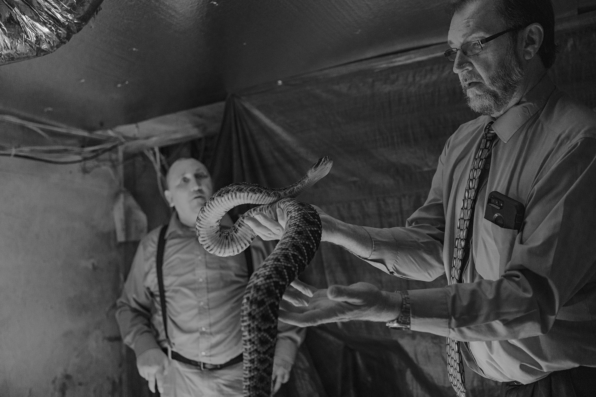 a man holding a large snake while another man looks on