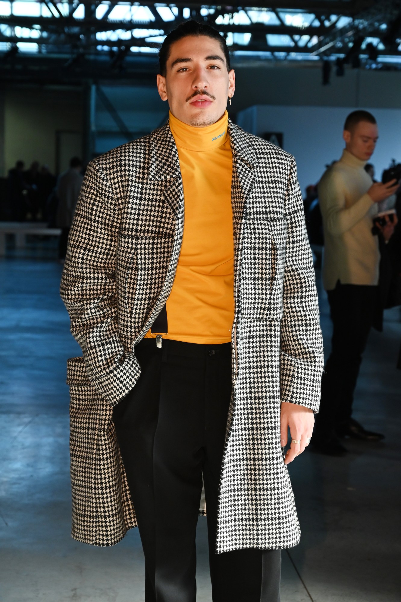 Hector Bellerin wearing a houndstooth coat and mustard jumper at a show during Milan Fashion Week