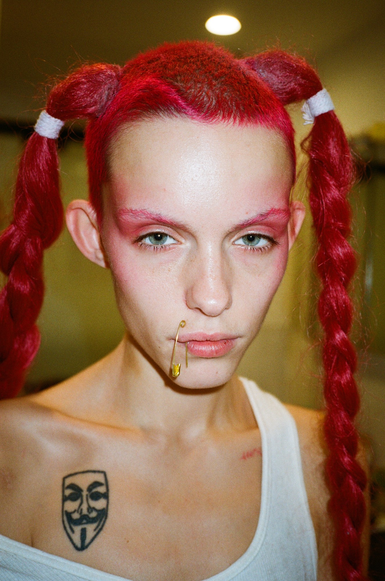 a woman with dyed red hair in pigtails and a safety pin through their lip