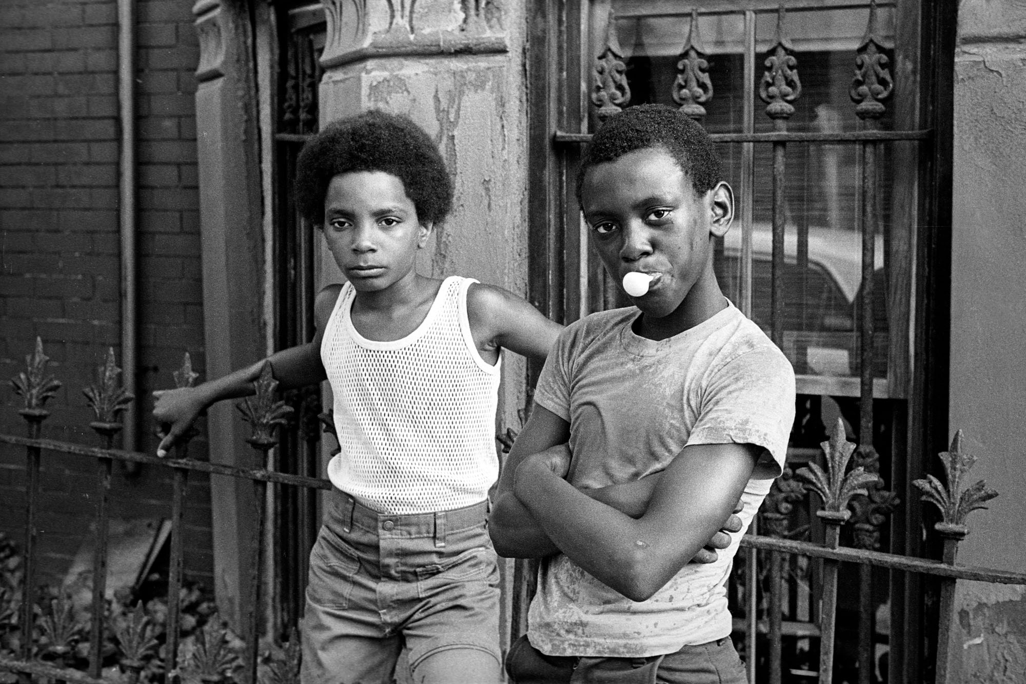 two boys leaning against a railing, one blowing bubble gum