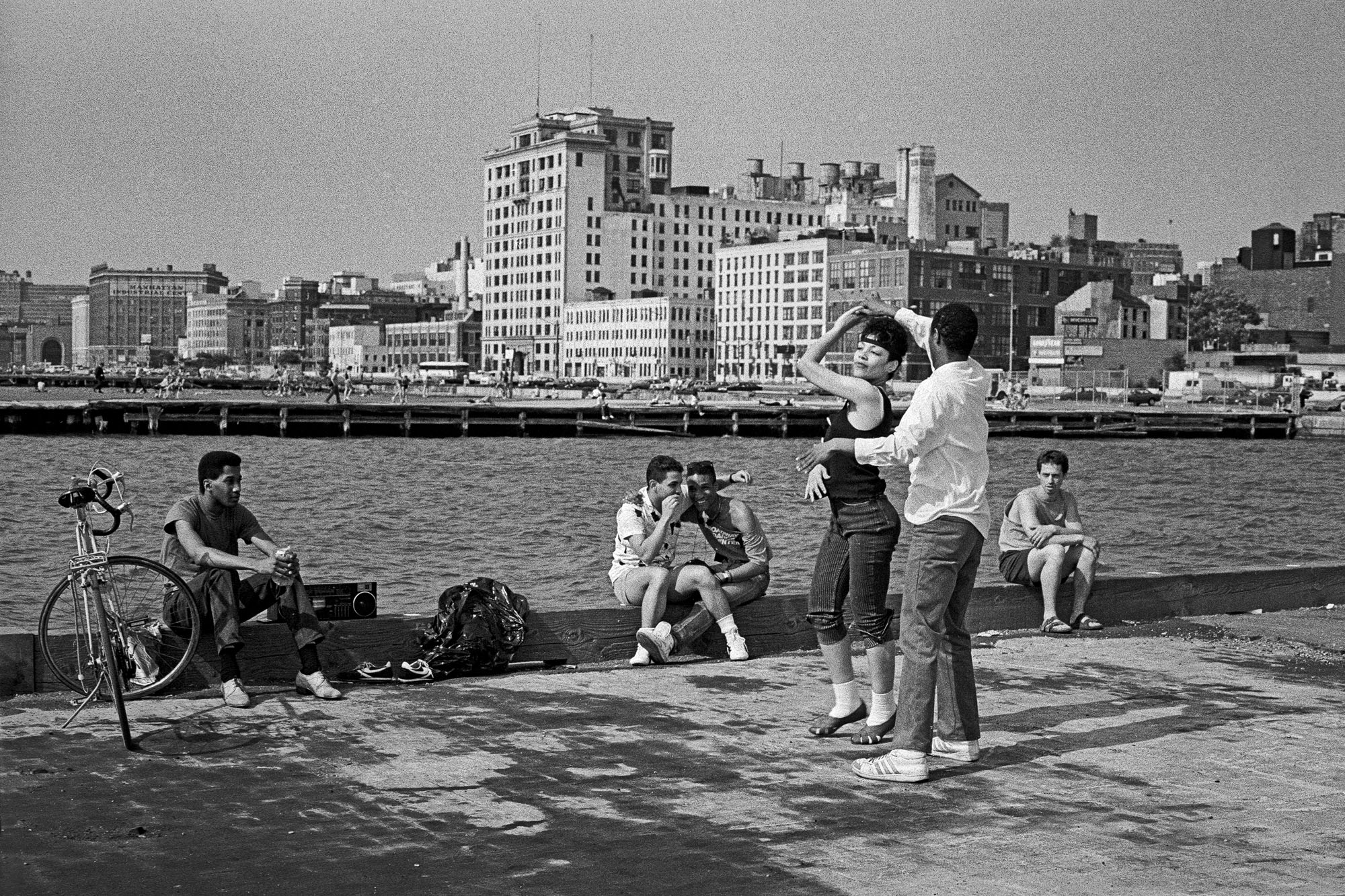 a man and woman dance in front of people sat by the river