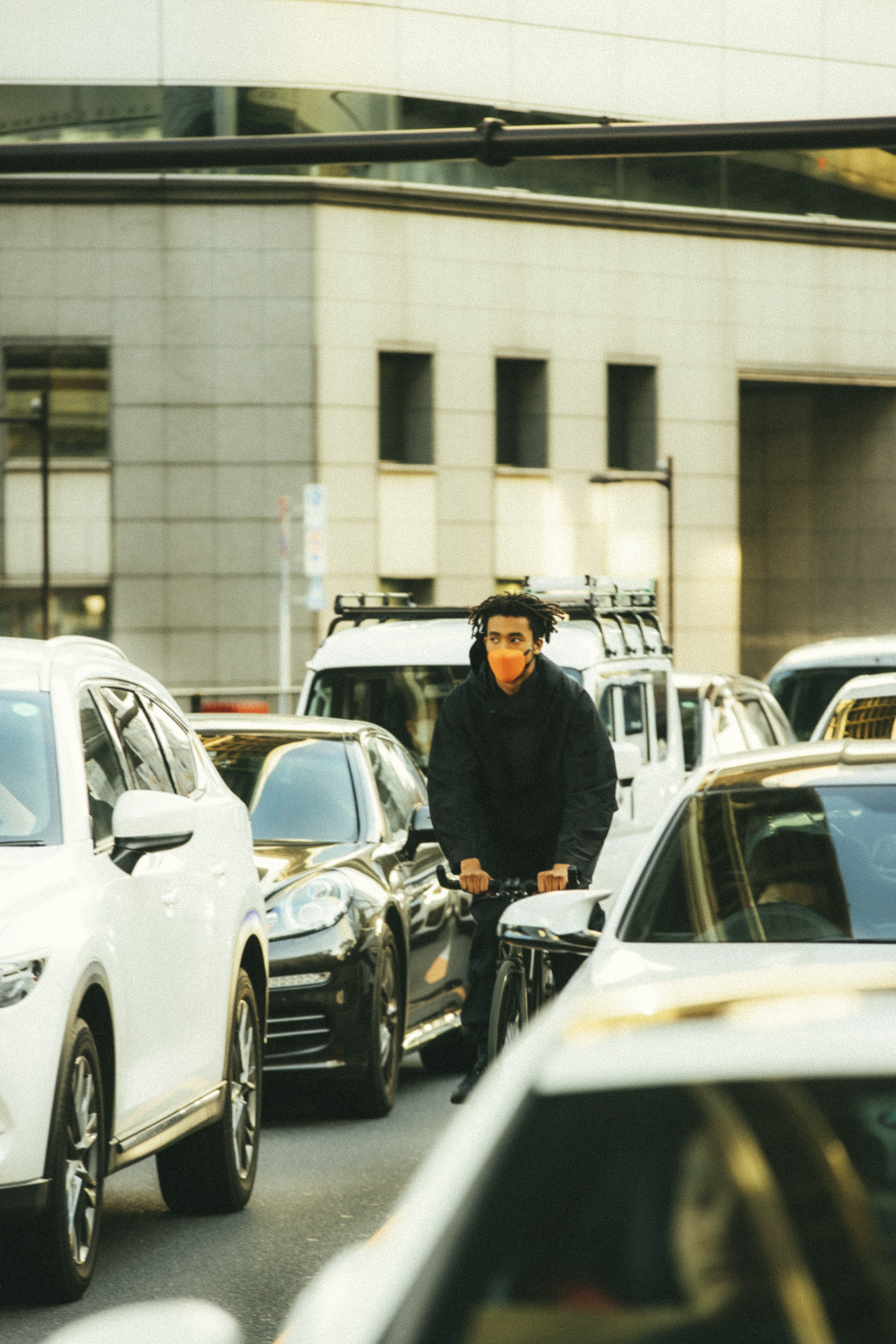 A model cycling between cars on a busy street wearing a face mask by Masuku