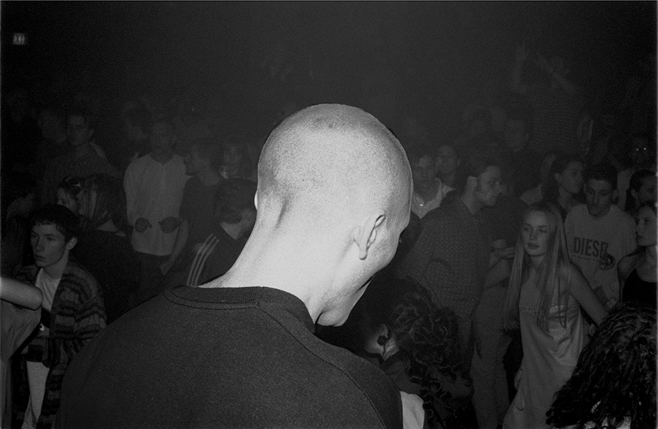 a man's shaved head in the foreground, dancers in the background