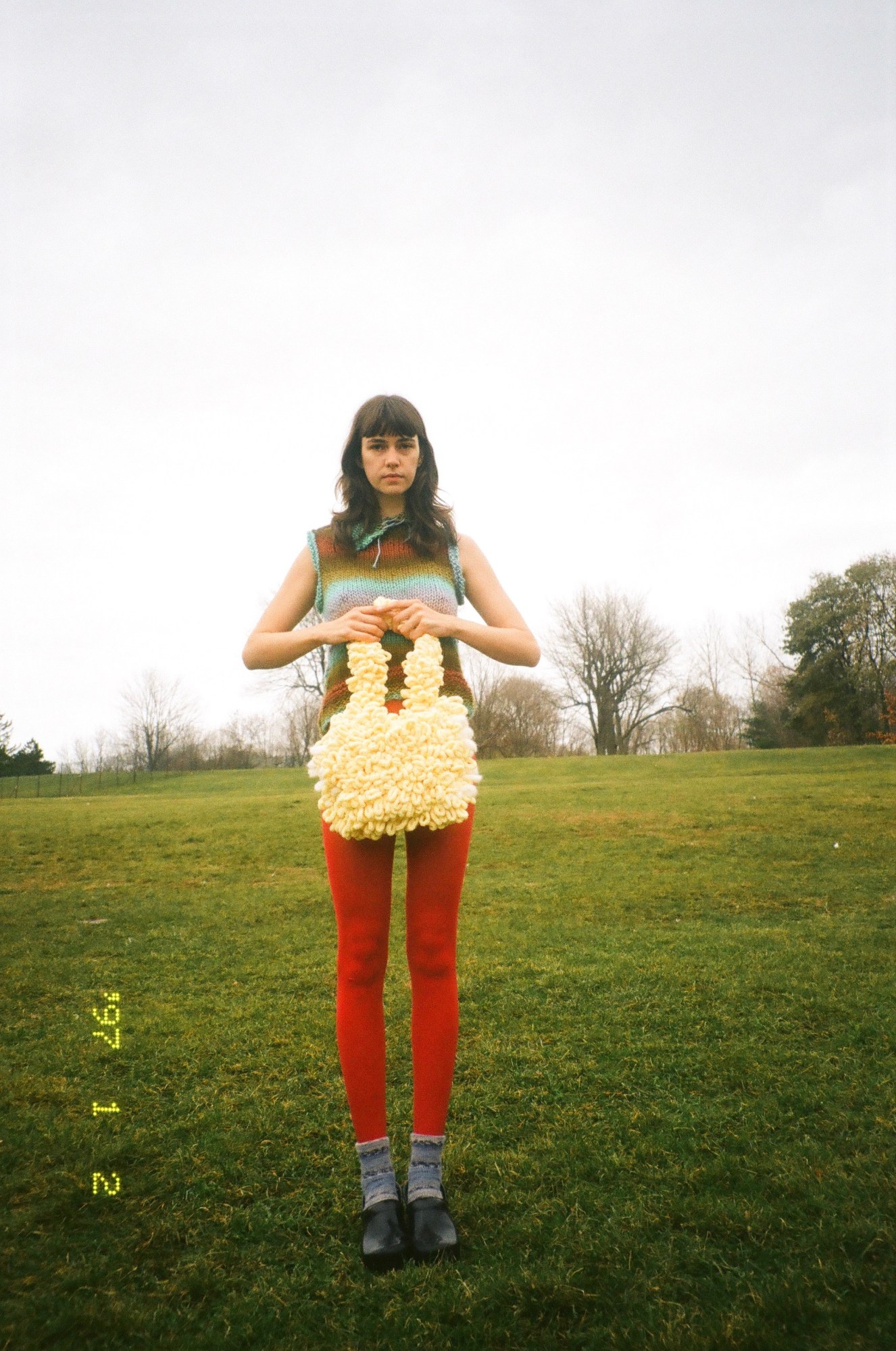 model carrying a canta woven bag in a grassy field