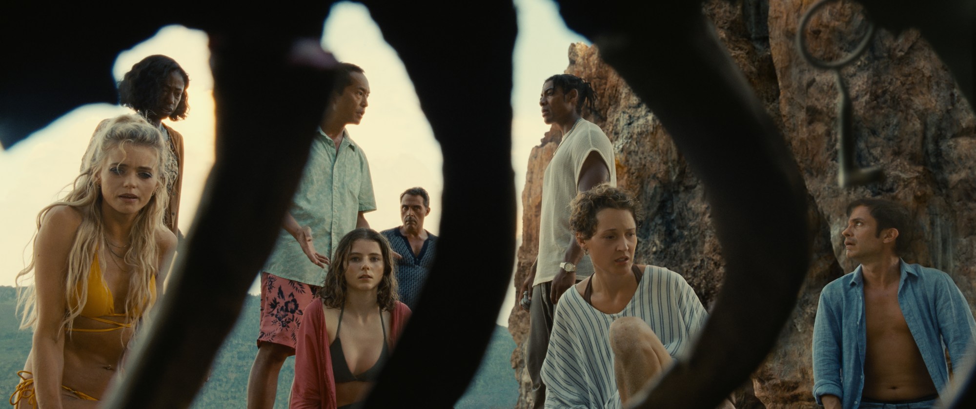 The beachgoers stare at the remains of a human body, peeking through the ribcage as they discuss how to save their own fates.