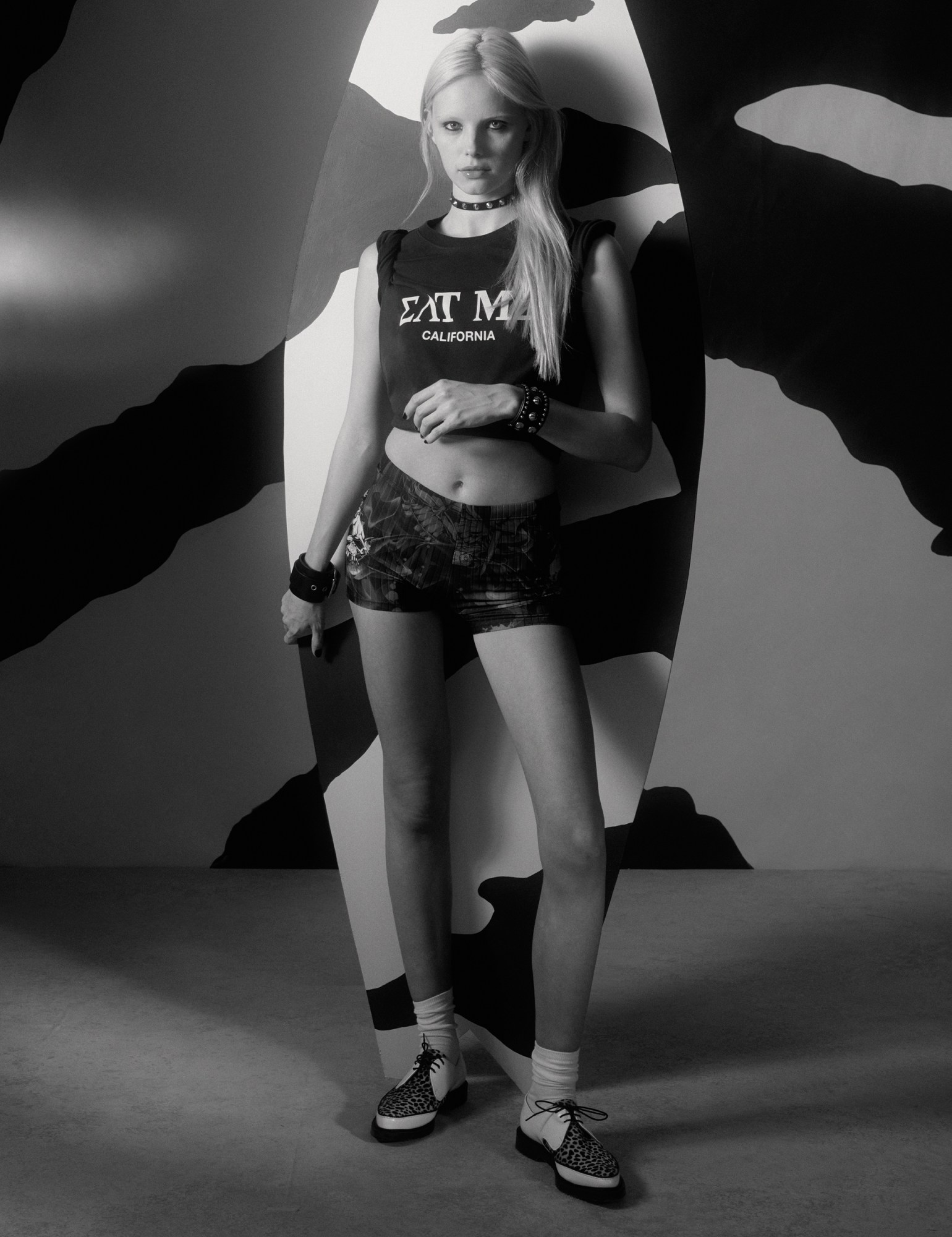 a model standing against a surfboard in short shorts and an 'EAT ME' t-shirt