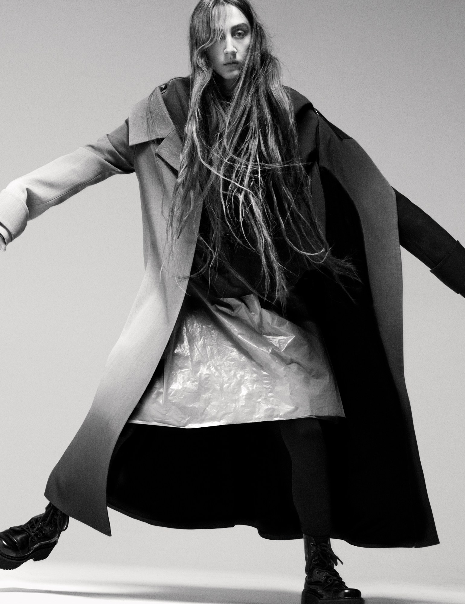 a model with long hair looks to camera wearing an oversized coat and shiny plastic-look skirt