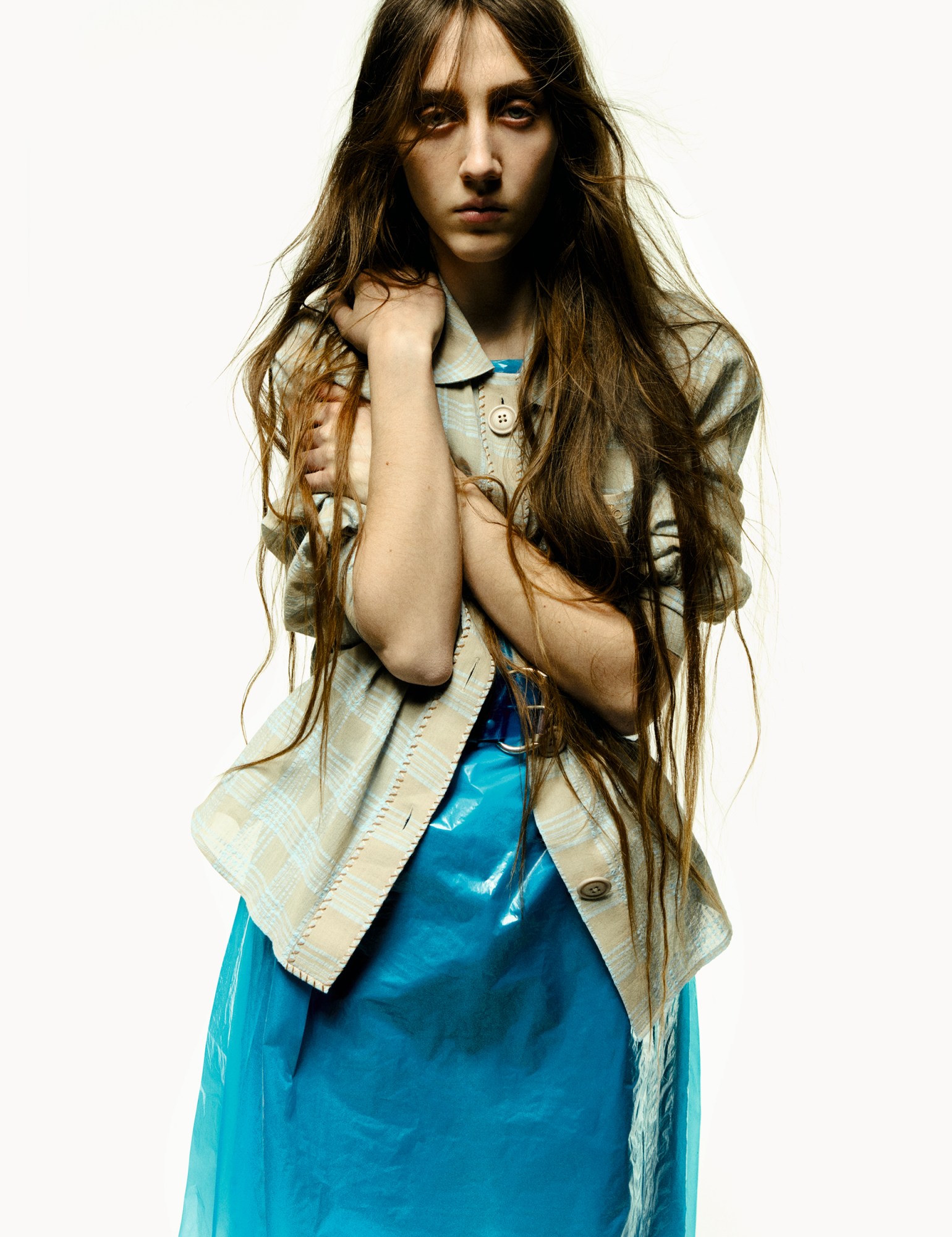 a model with long hair wears a bright blue PVC dress with a checked shirt over it