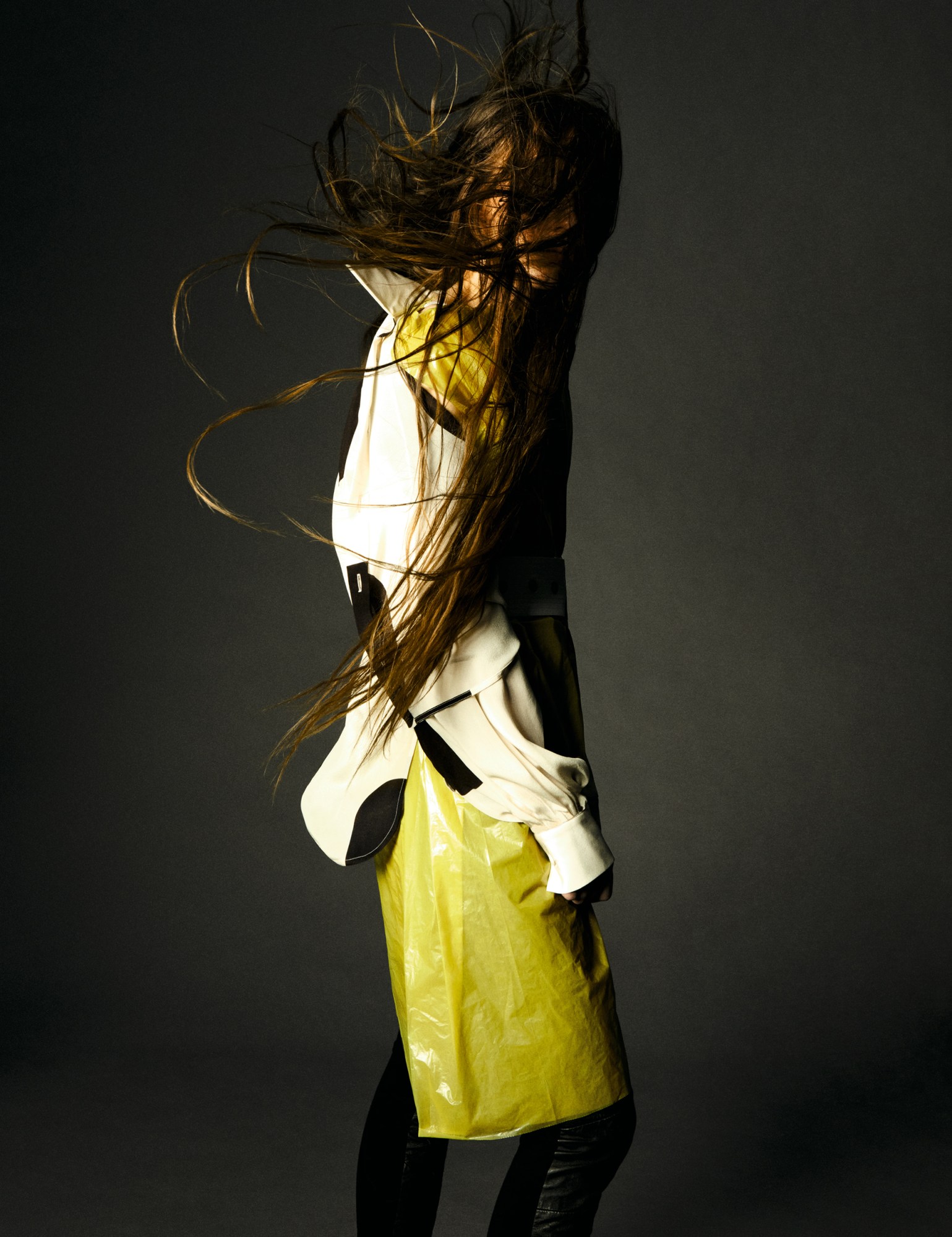 a model stands sideways in a studio, their hip-length hair blows in all directions, obscuring their face