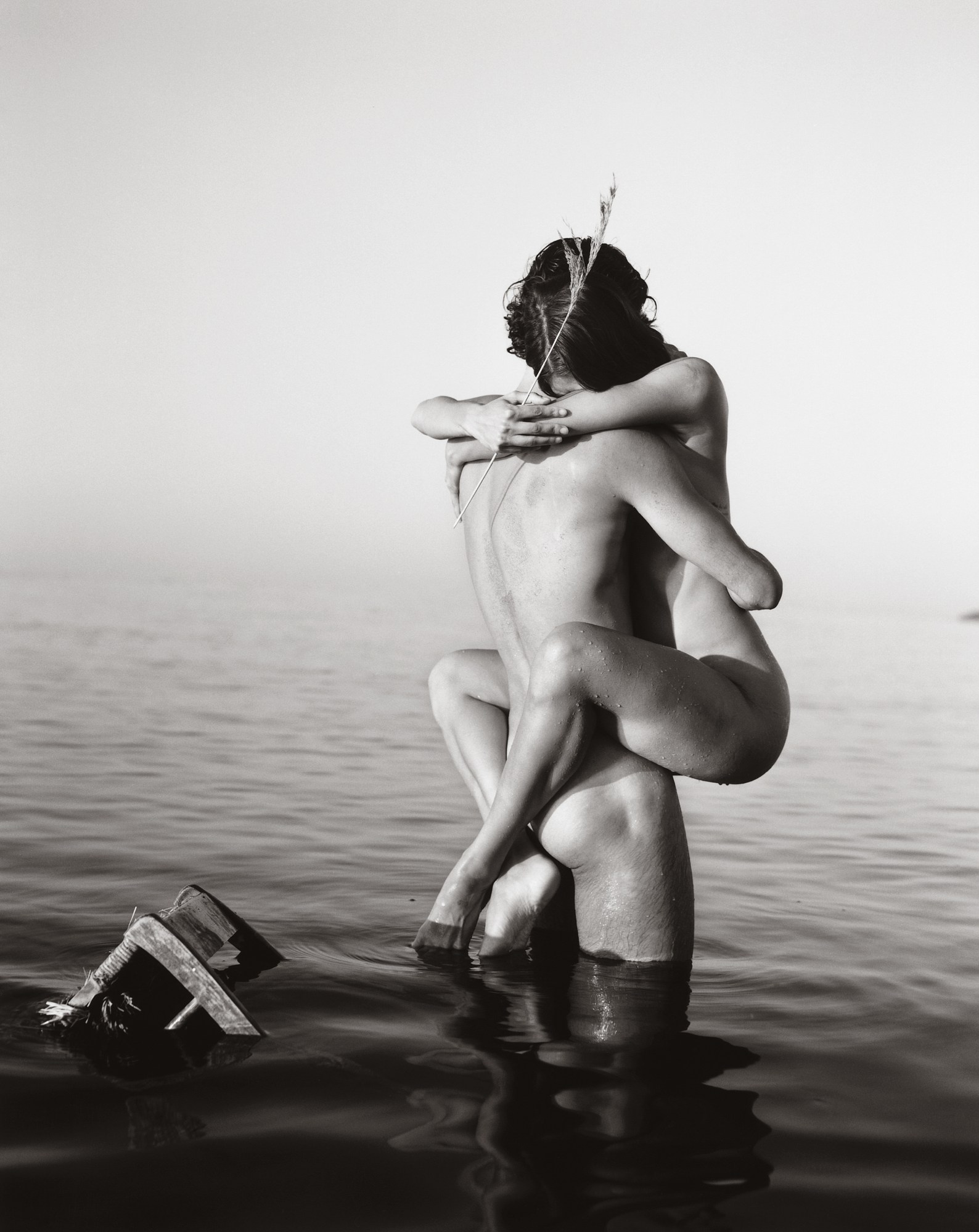 a naked woman wraps her legs around a naked man stood in a lake