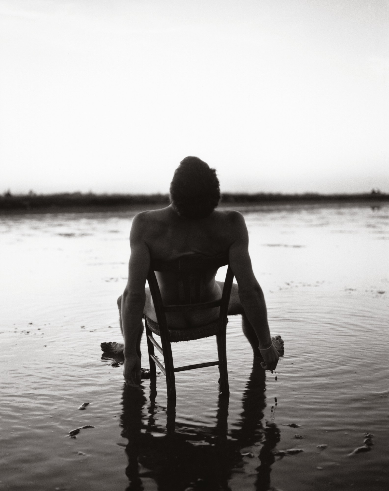 a man sat with his legs wide open on a chair in a lake from the back