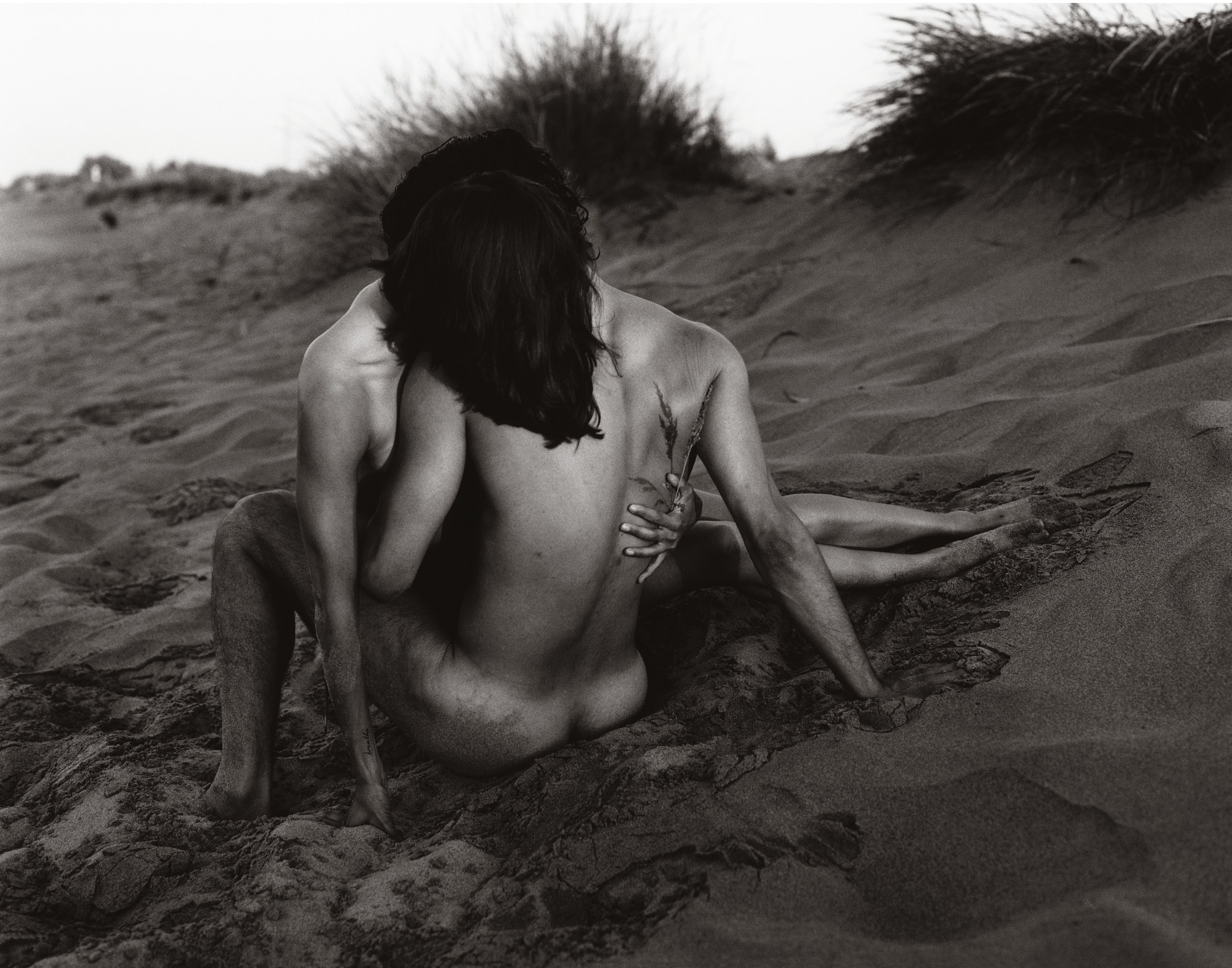 a naked man and woman embracing in sand