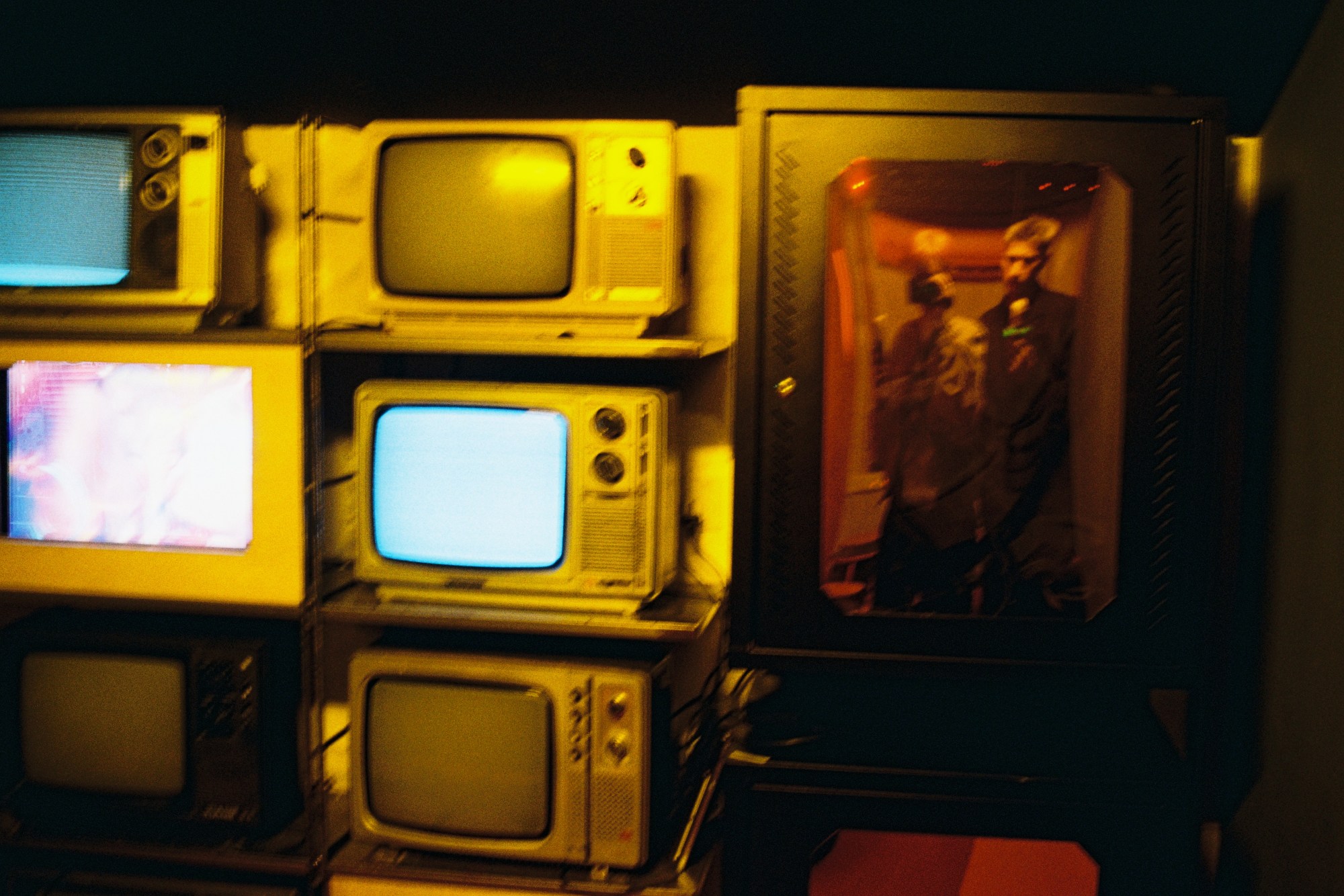 Two people take a photo in the reflection of a TV in an old small TV shop.