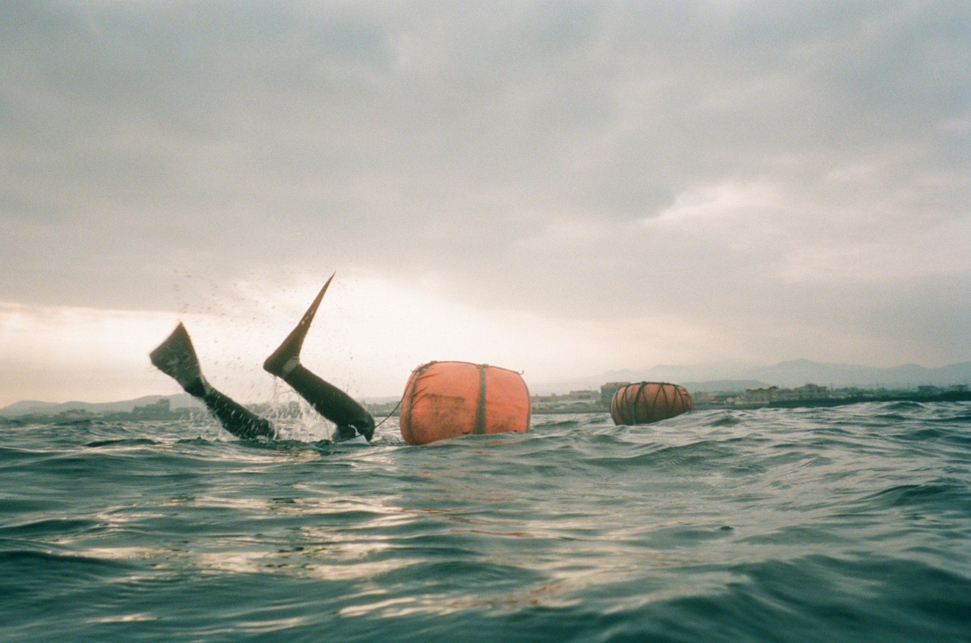 Diver's legs sticking out of the ocean as they go in. Faintly in the background you can see the mountains.