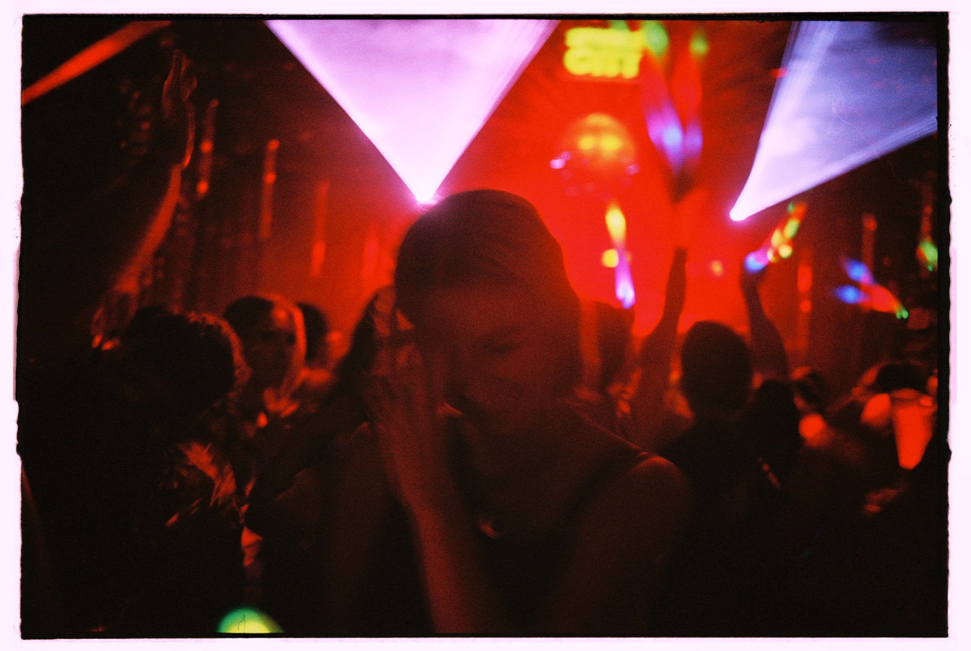 A woman takes a photo of herself in front of a crowd with their arms raised as they look at a stage and strobe lights go over them.