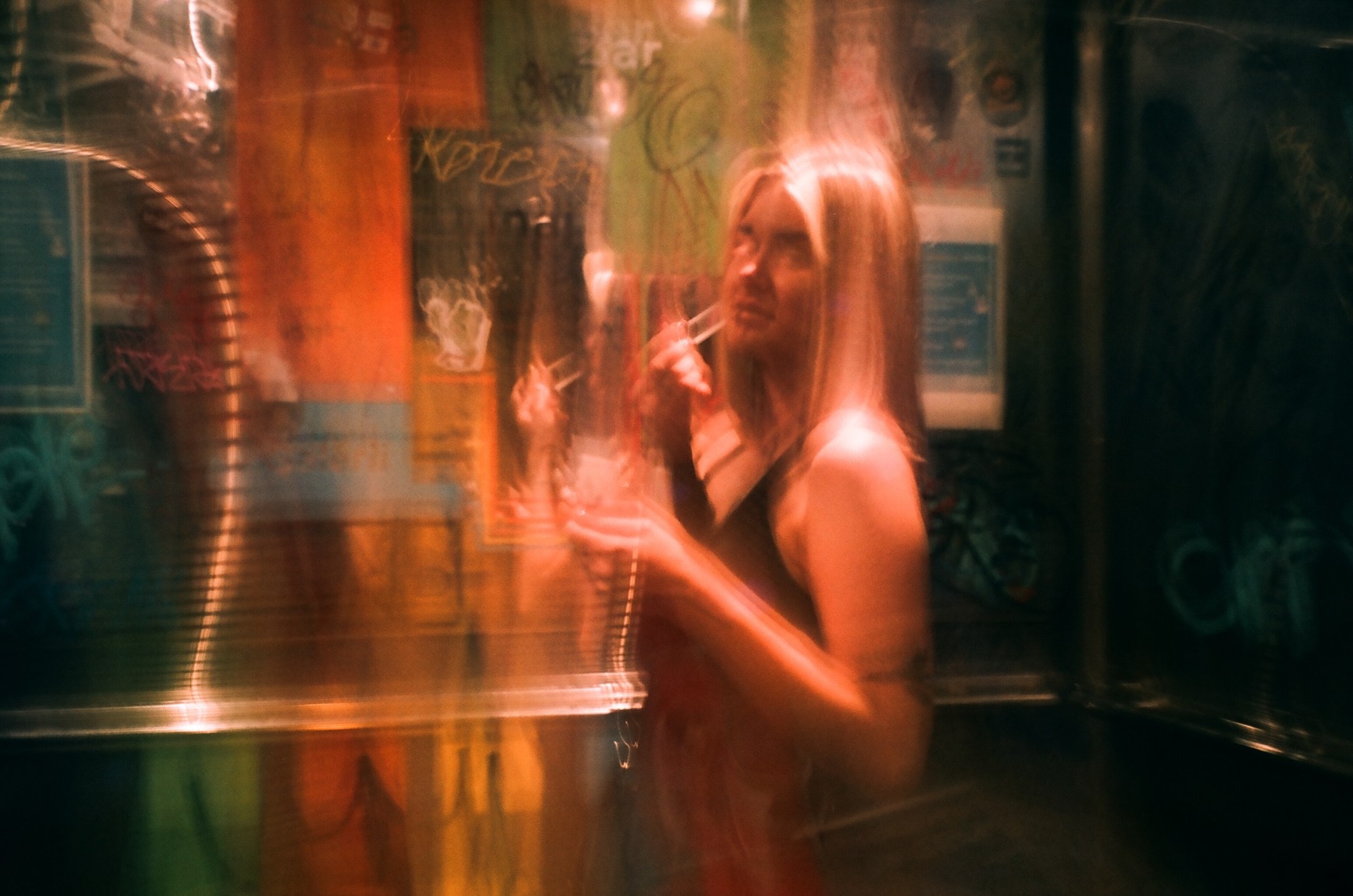 A blurred photo of a blonde girl putting on a makeup. In the background is club posters and string lights.