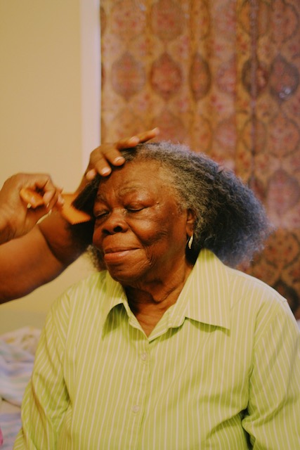 A woman in a green stripe shirt has her hair brushed with a comb.