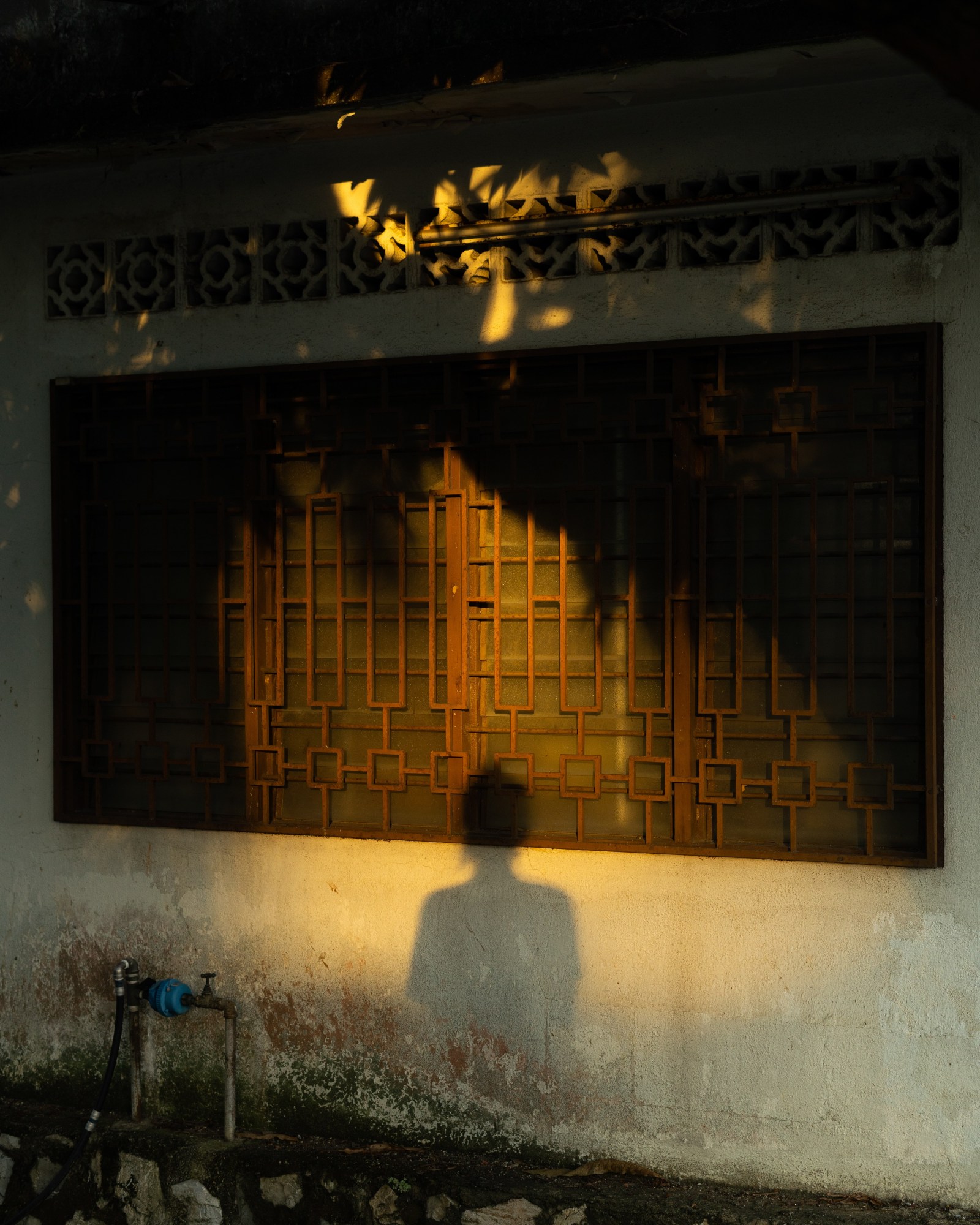 The shadow of a woman against on outdoor wall with a hose tap and window.