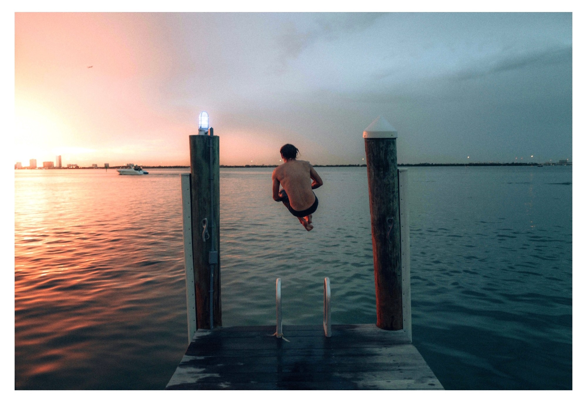 a man canonballing off a jetty at sunset